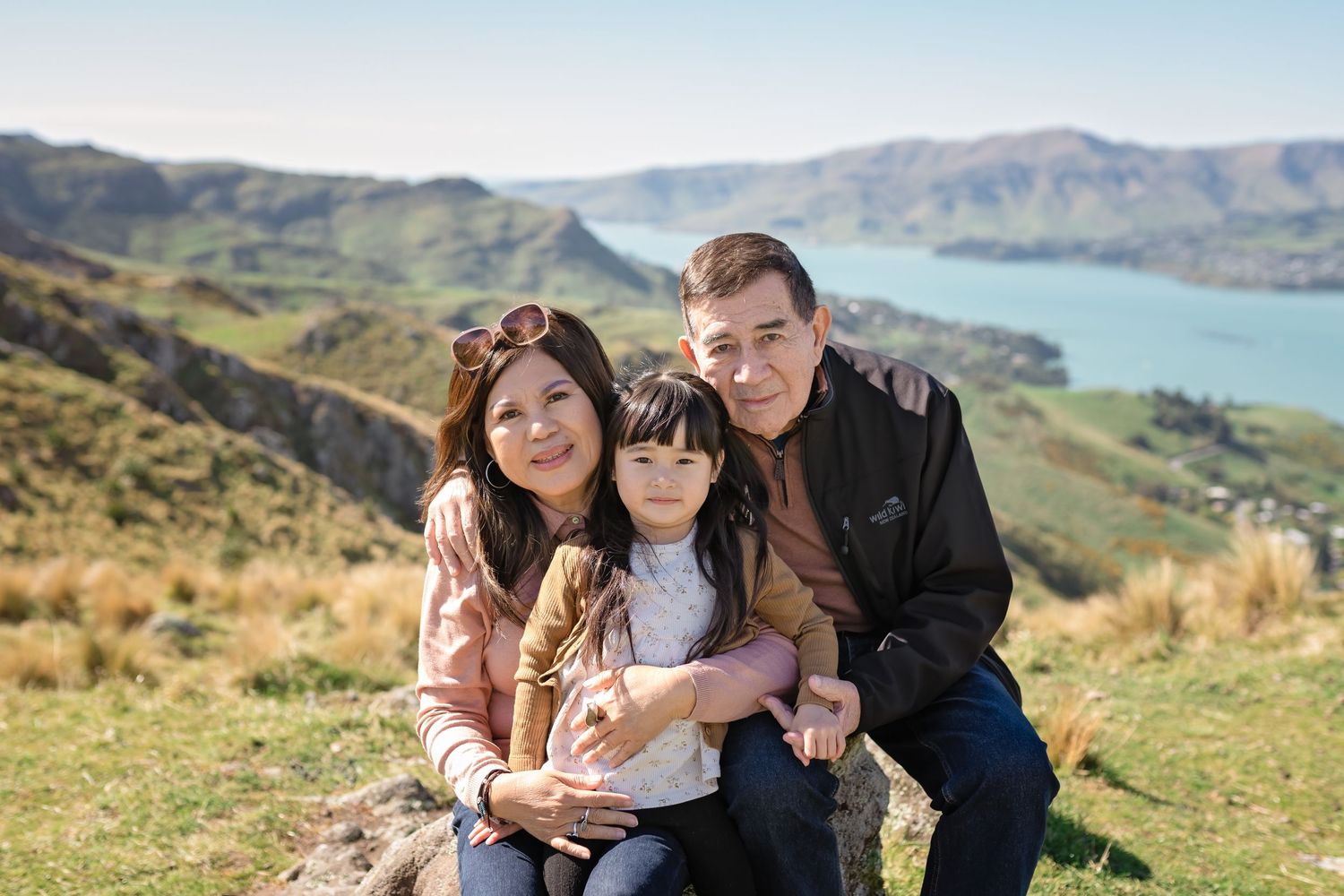 A happy family enjoys quality time together while sitting on a grassy hillside overlooking scenic mountain views.