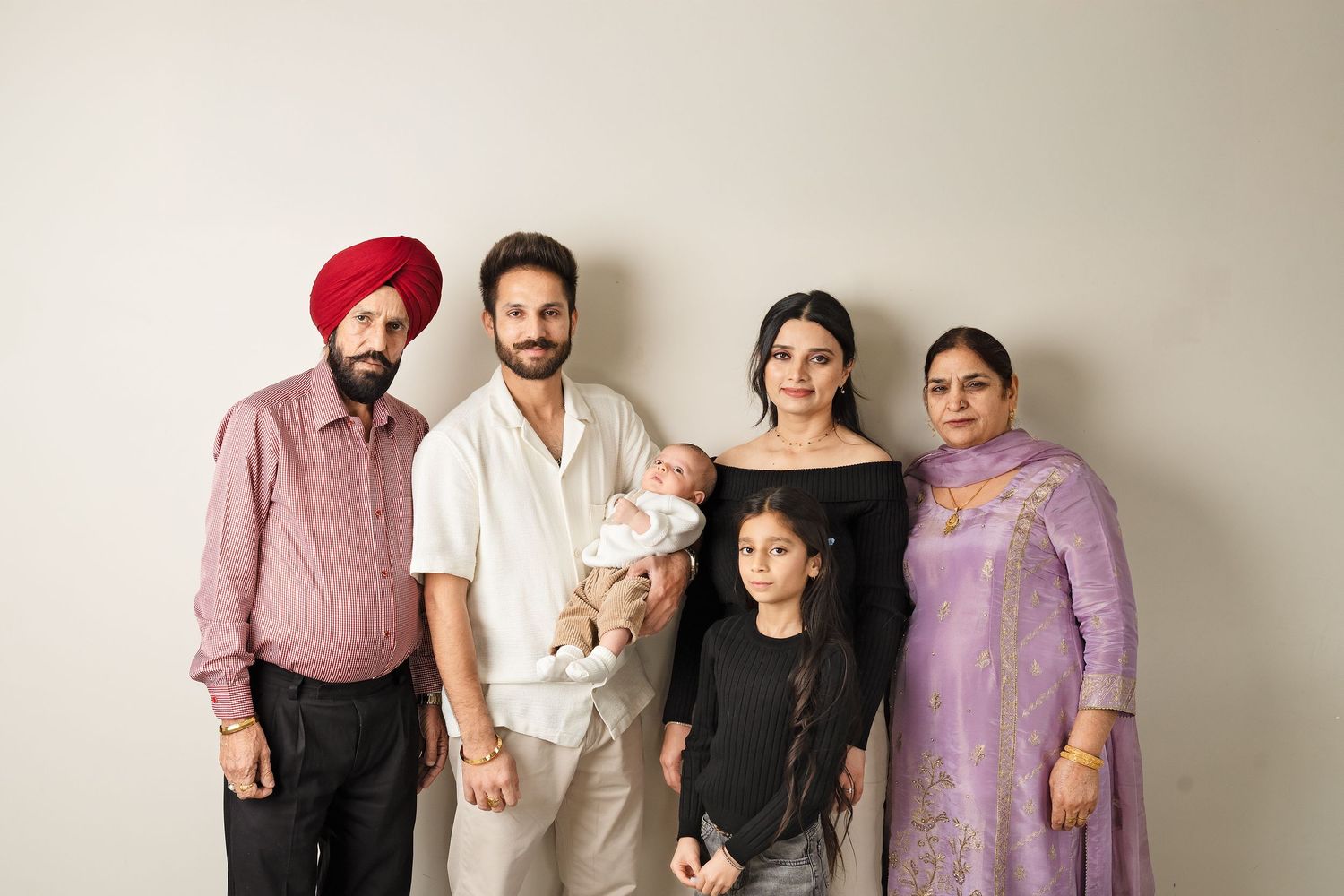 Multi-generational family group standing together against neutral background in studio setting.
