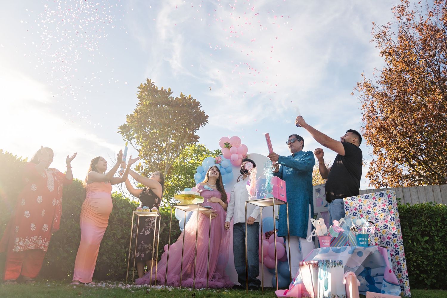 Wedding party members hold flower petals and rose bouquets while wearing pink and blue formal attire during an outdoor celebration.