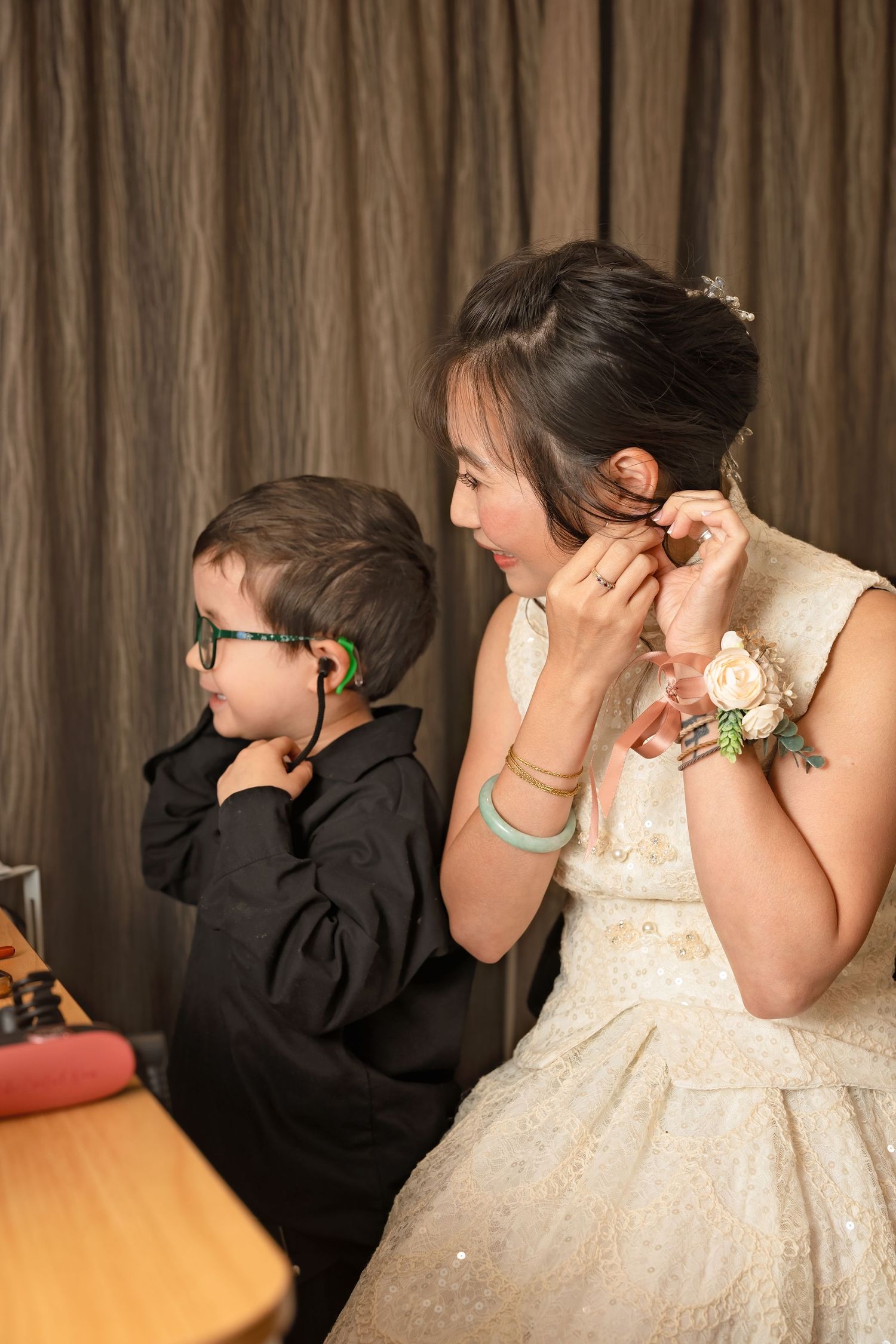 Bridesmaid and young boy putting on earrings and tie before wedding ceremony.