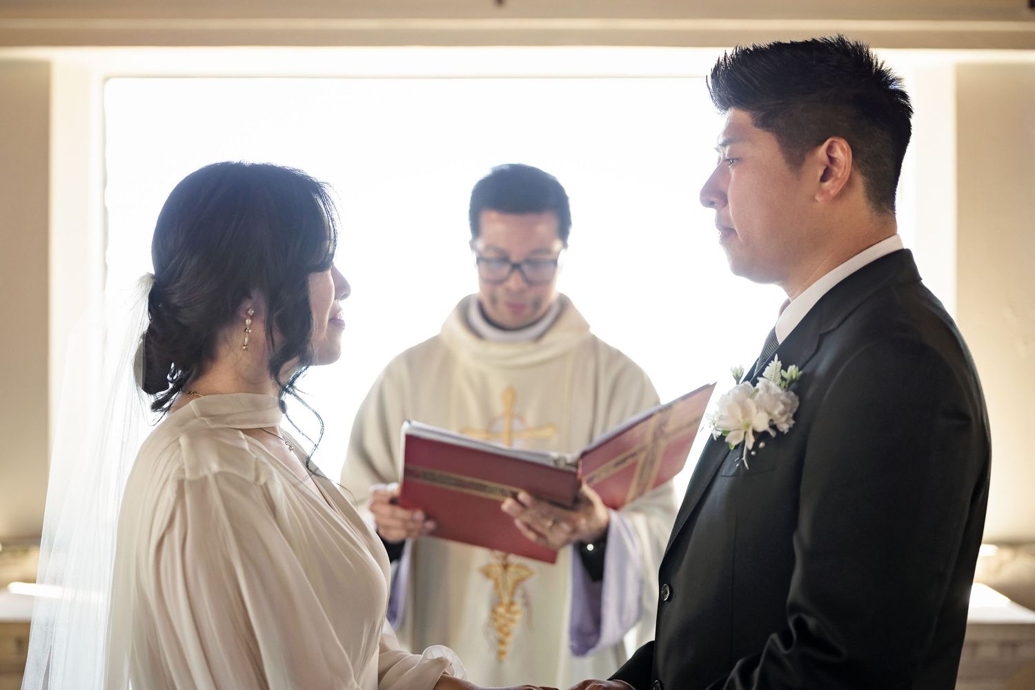 Bride and groom face each other during intimate wedding ceremony with priest officiating.