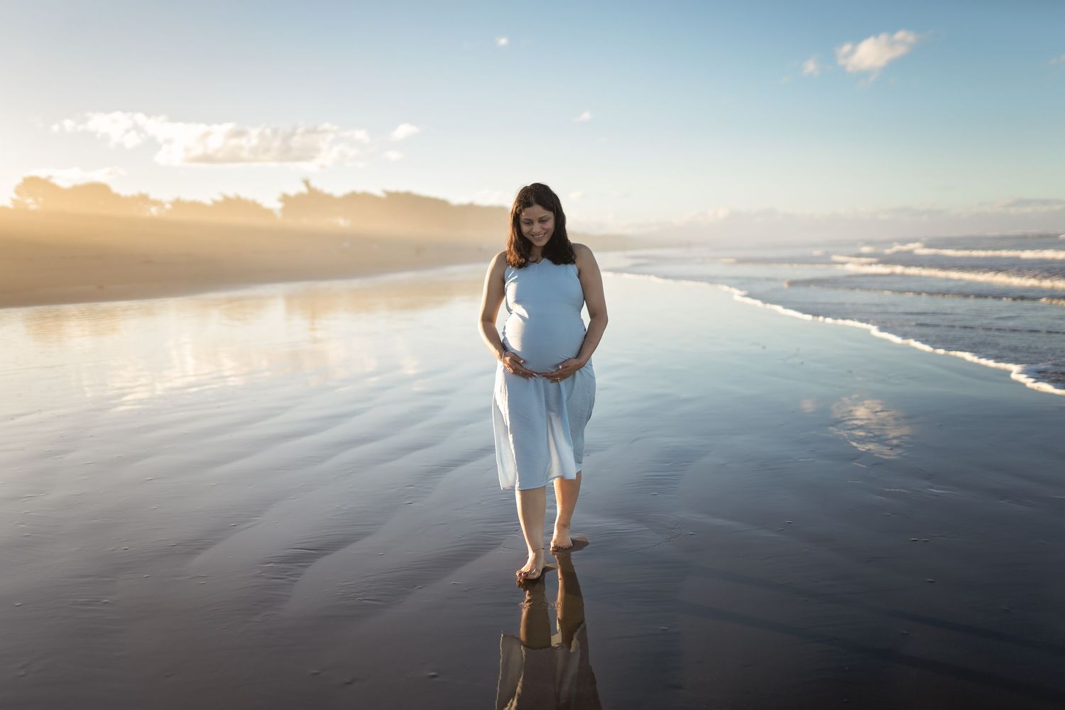 Silhouette of person standing on tranquil beach at sunset with rippling ocean water and calm atmosphere.