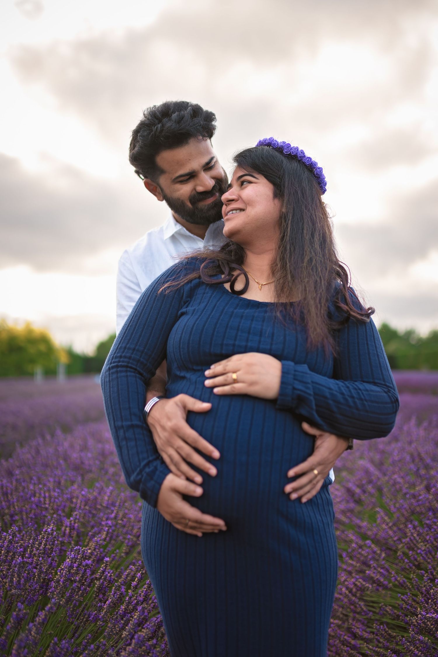 Couple embracing in a purple lavender field during a maternity photoshoot.