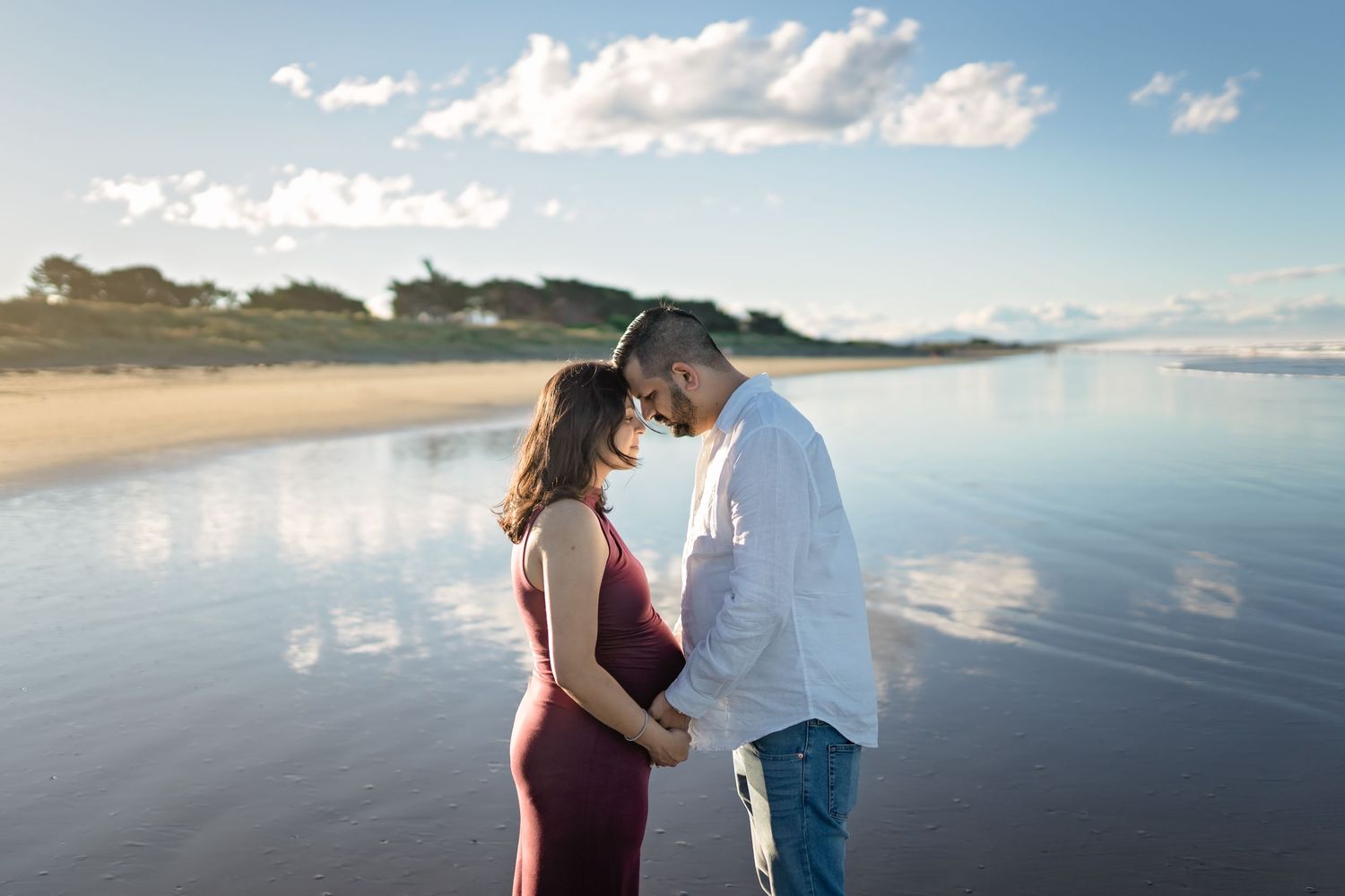 Couple walking together in romantic beach photo session at sunset with ocean waves and cloudy sky.