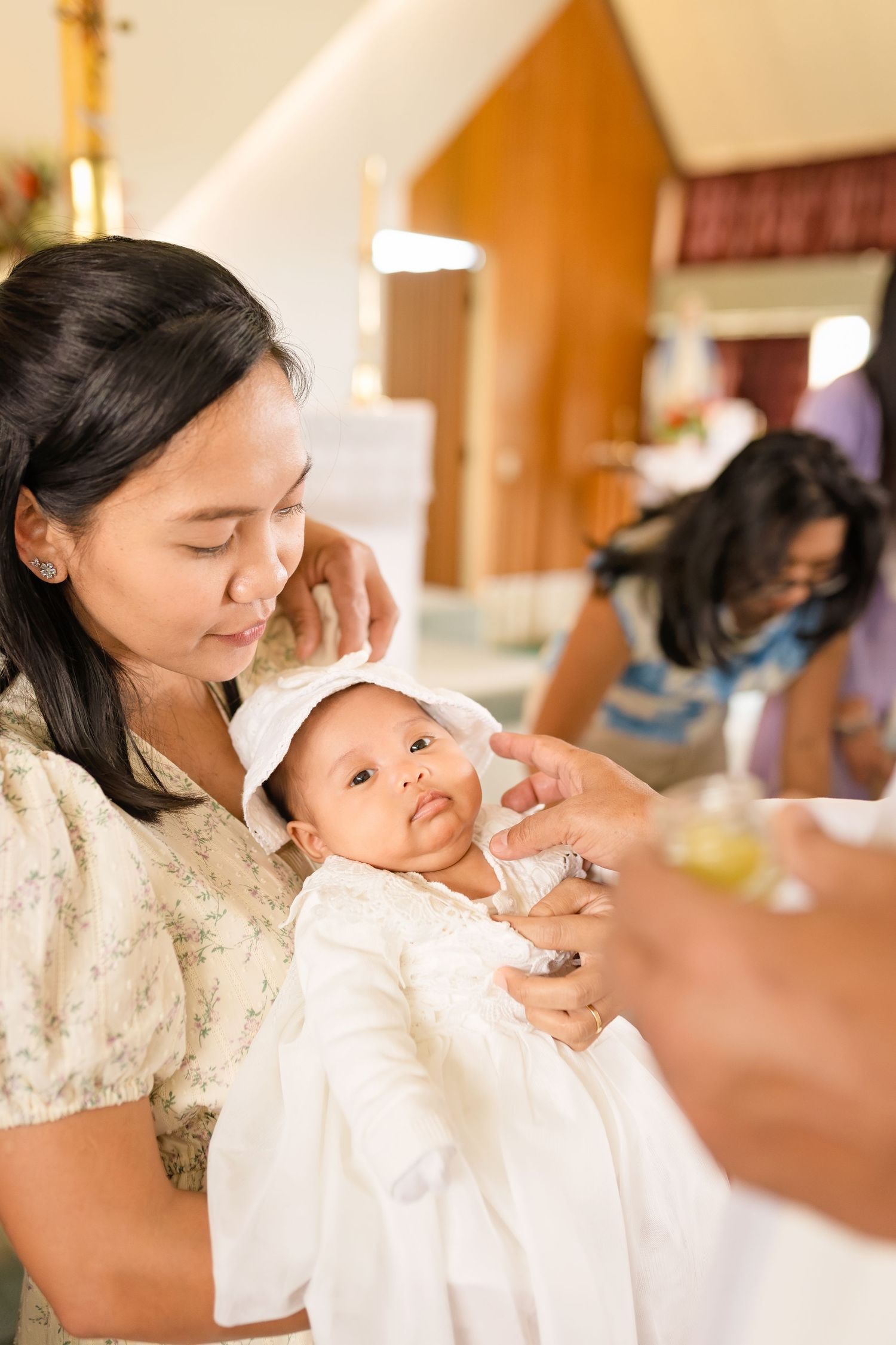 Mother holds baby in white christening gown during baptism ceremony in church.