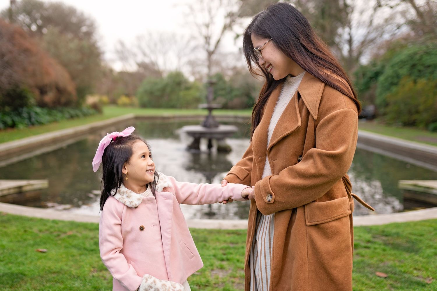 A parent and child share tender moments outdoors in autumn wearing coordinating pink and brown coats.