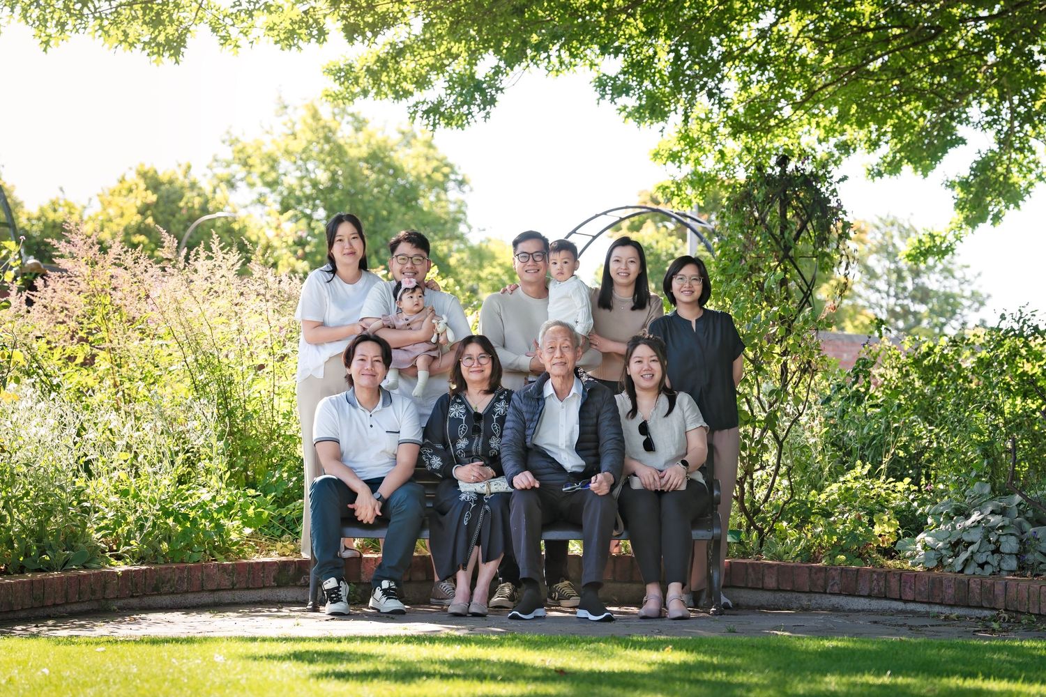 Group of people sitting outdoors on stone steps surrounded by lush green trees and landscaping.