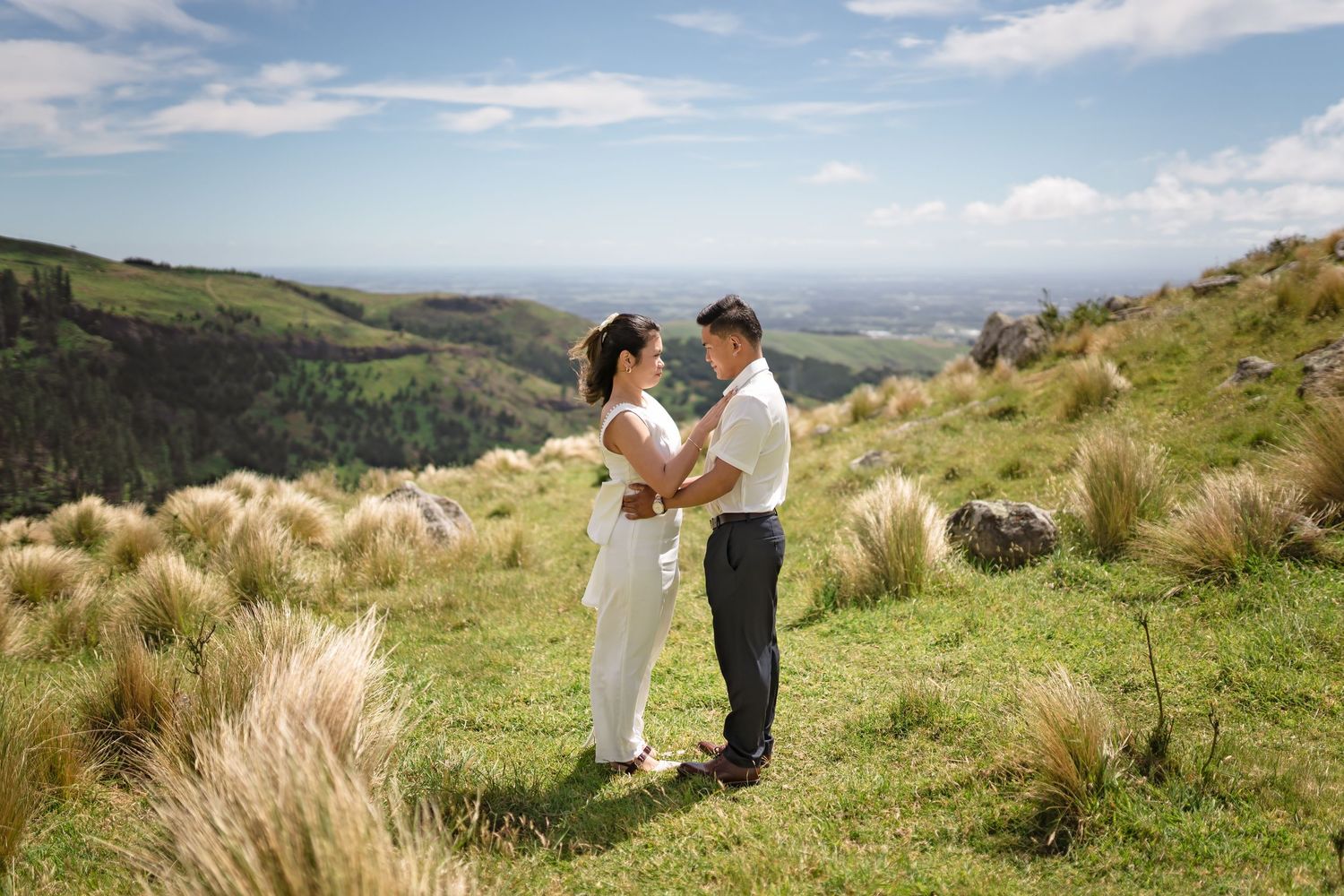 Couple sharing a romantic moment on a lush green hillside with panoramic valley views on their wedding day.