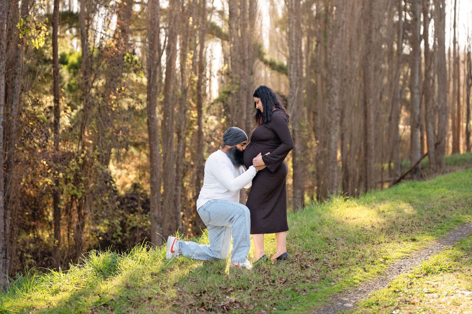 A man kneeling before a woman in hijab on a forest path, surrounded by tall trees in golden sunlight.