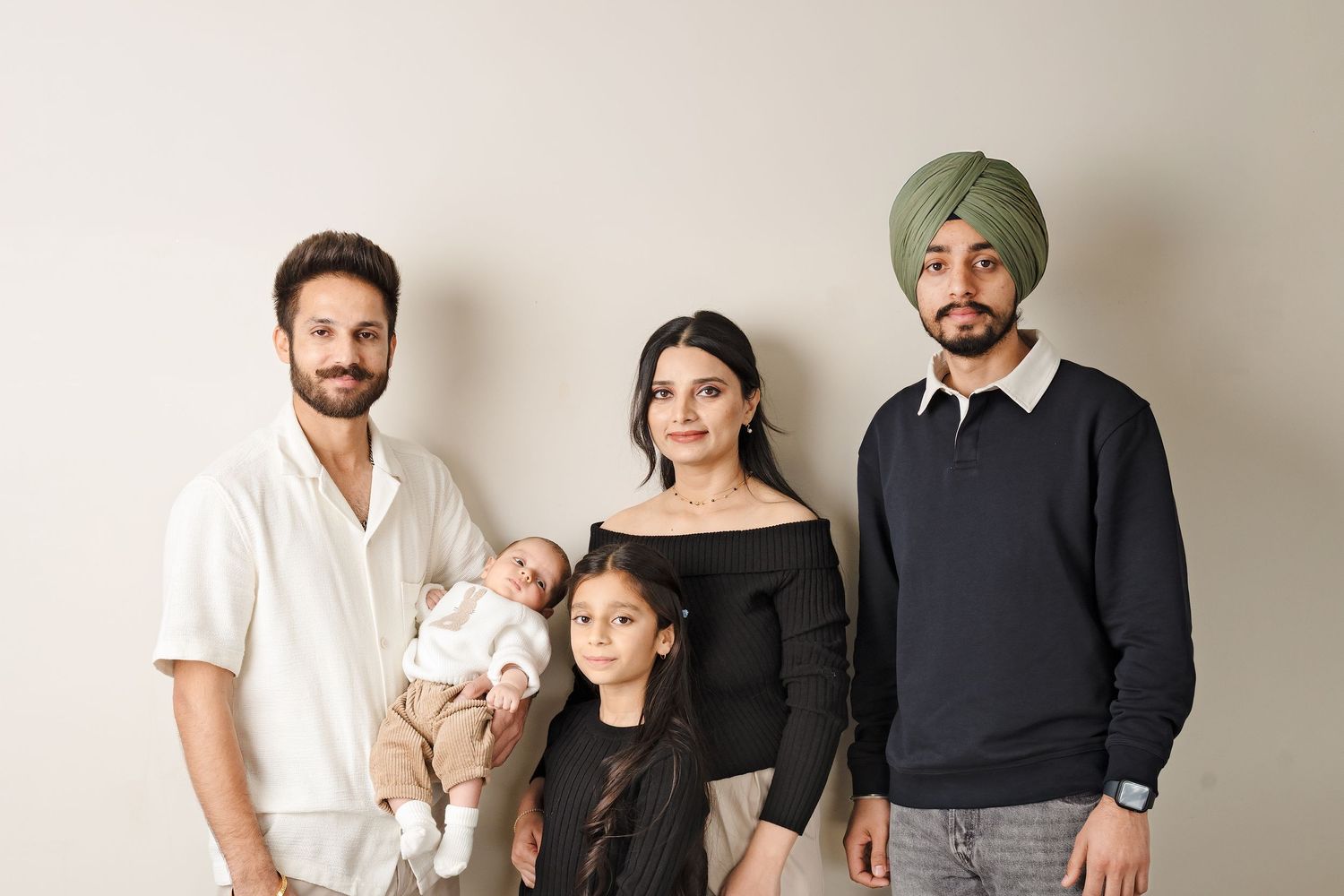 A family in coordinating black and white outfits poses together against a beige wall for a portrait.