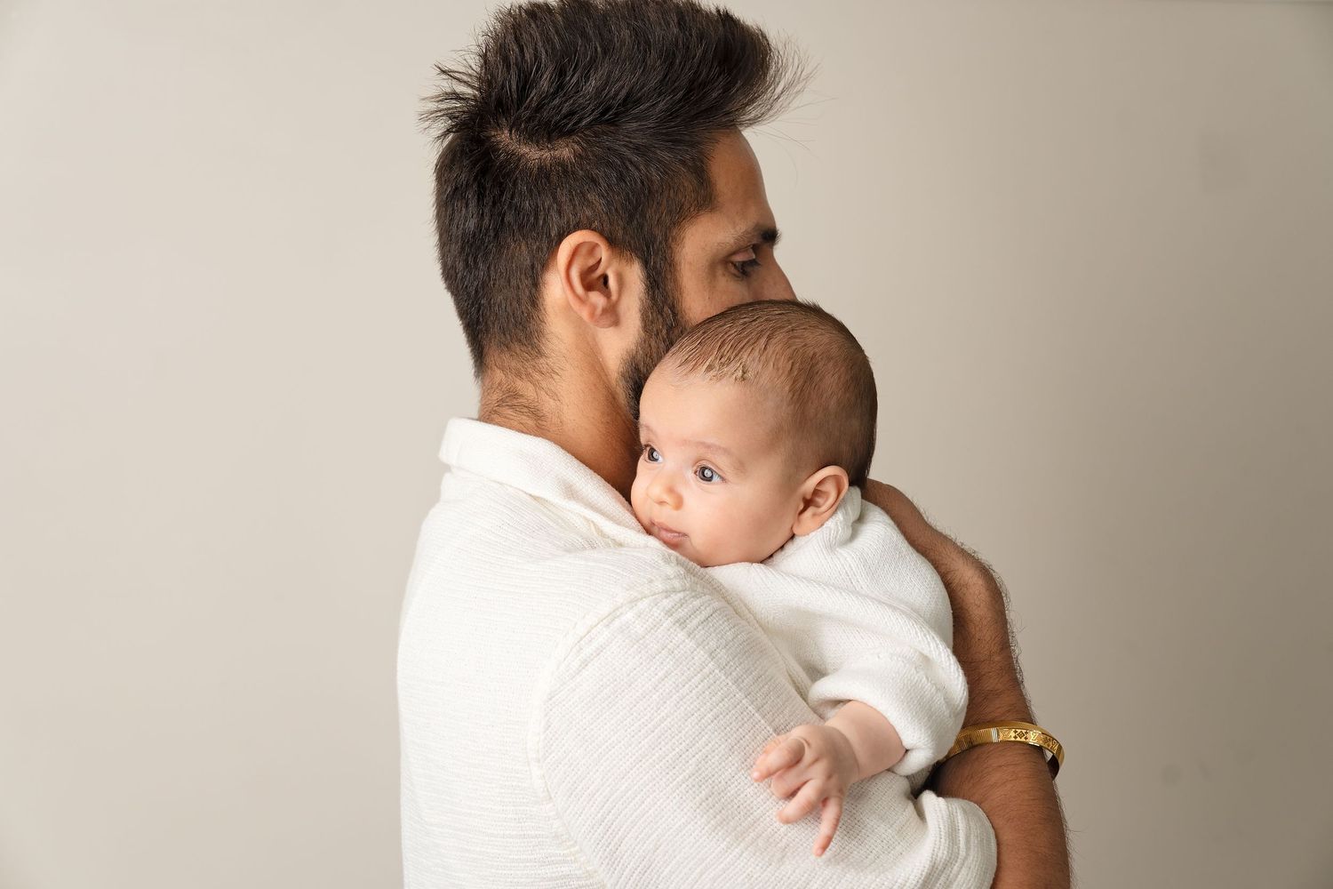 A comforting embrace between parent and baby in a white minimalist studio setting.