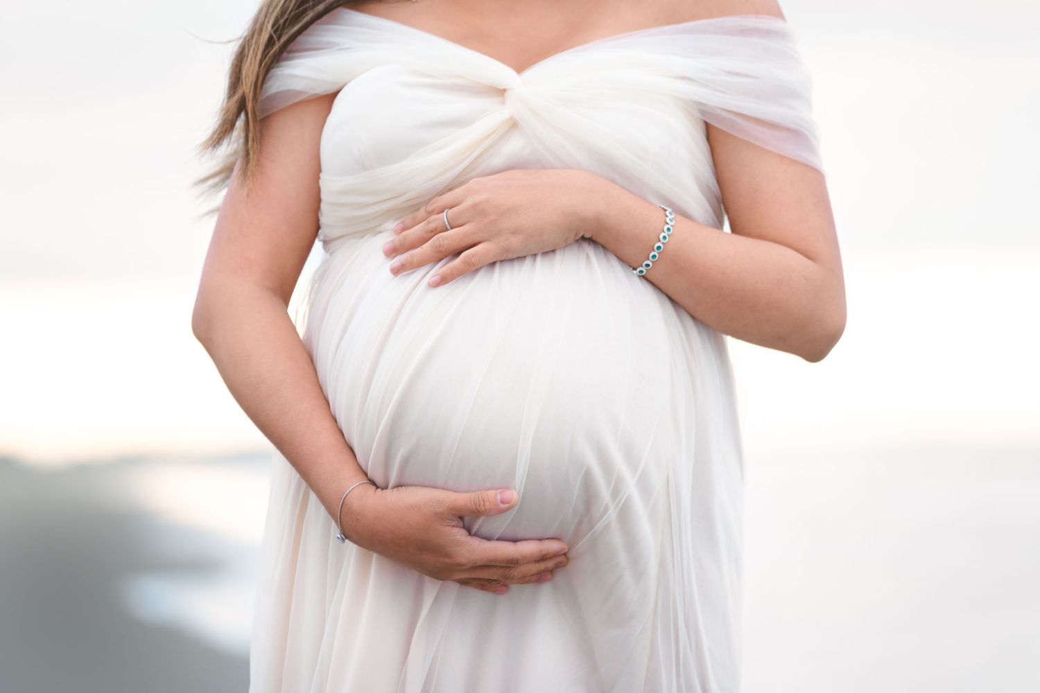 Elegant maternity portrait of woman in white dress highlighting her pregnant silhouette.