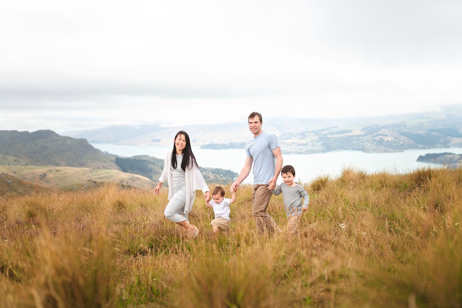 Family holding hands while hiking along a scenic mountain trail overlooking a lake.