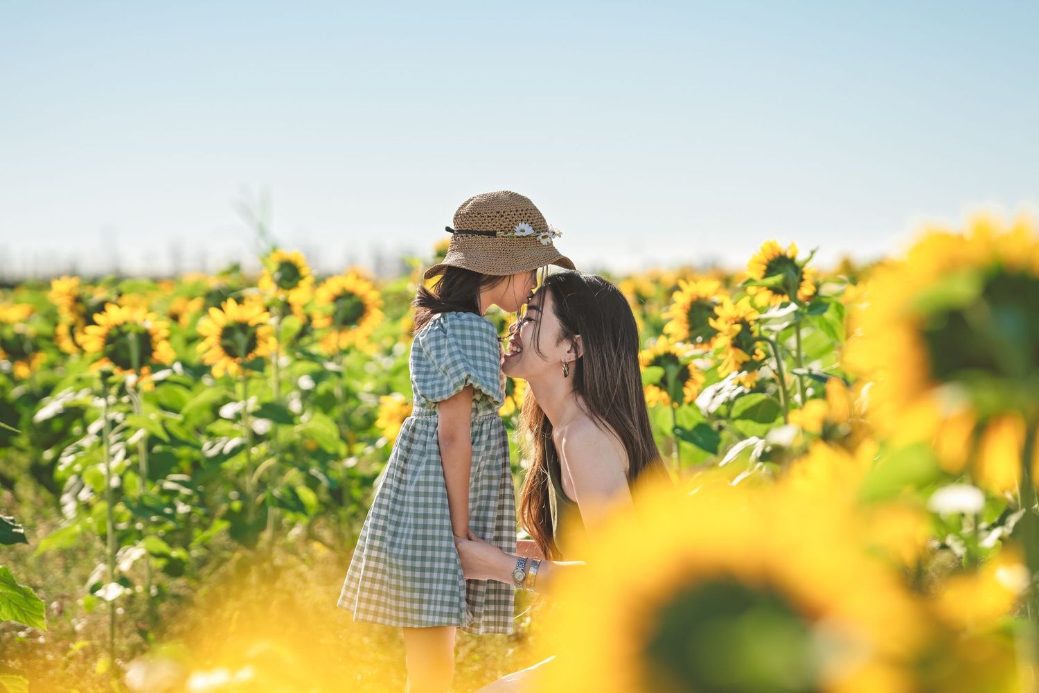 Mother and daughter share a tender moment among blooming sunflowers on a sunny day.