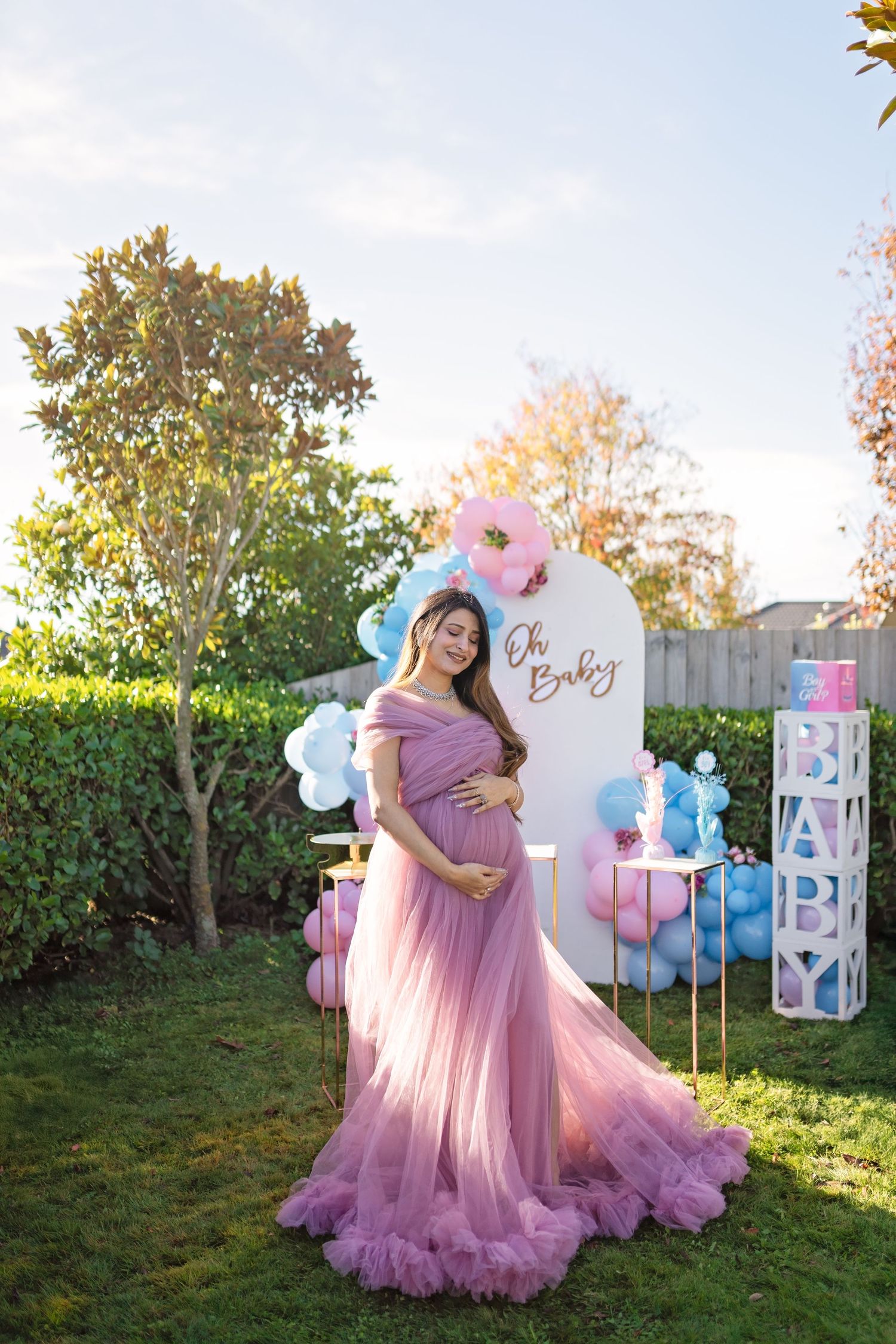 A baby shower celebration outdoors with pink tulle dress, balloon decorations and blocks display in a garden setting.