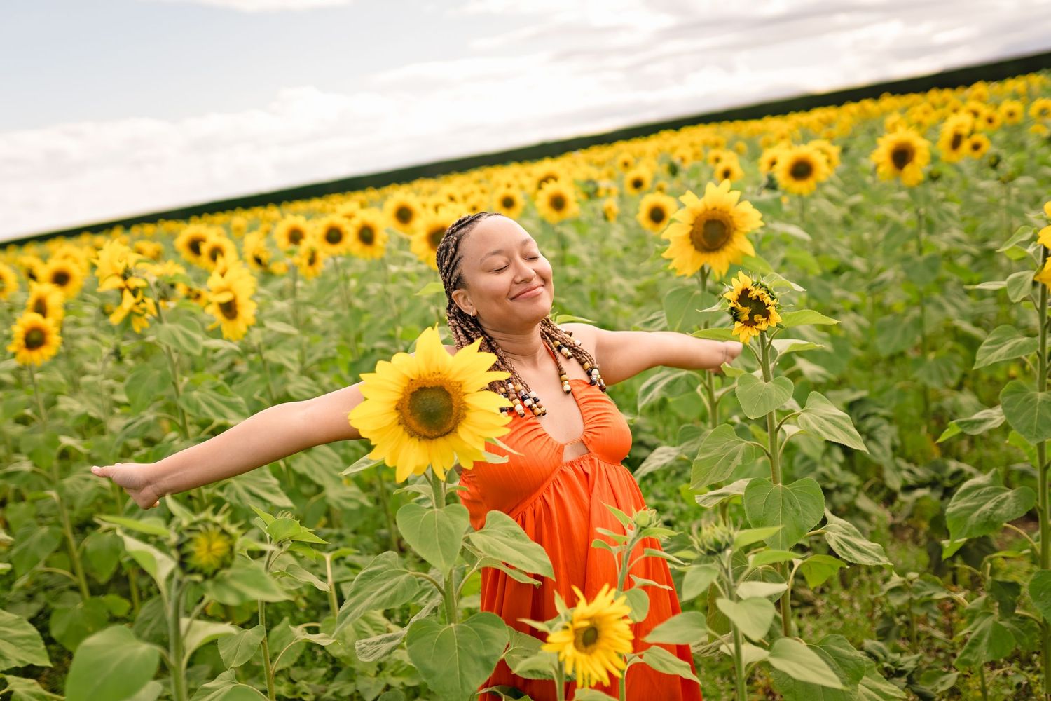 Joyful woman in orange dress with arms outstretched in a vibrant sunflower field.