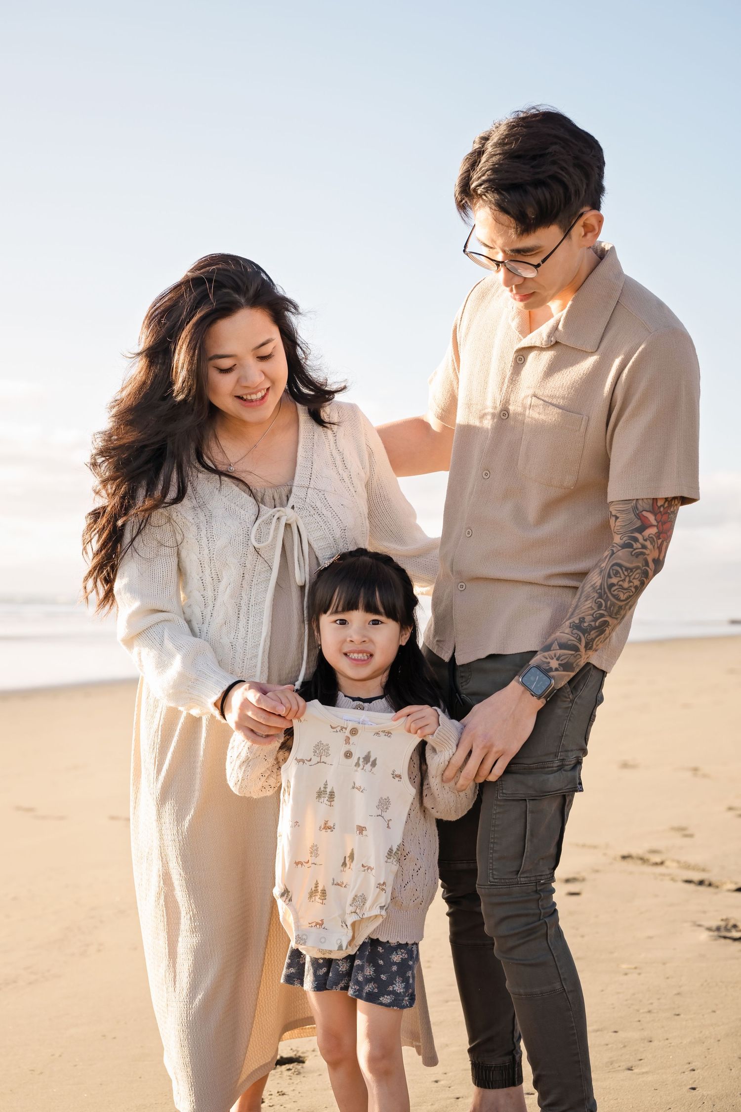 Happy family of three enjoying a sunny beach day, parents holding their young daughter's hands on the sandy shore.