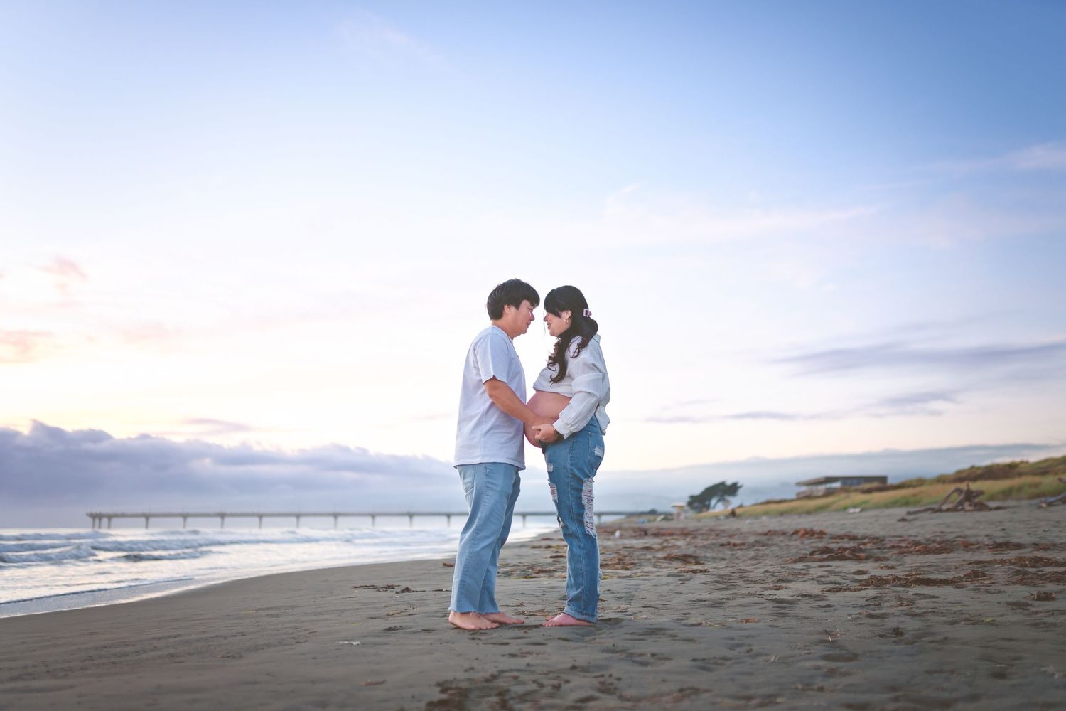 Intimate maternity moment captured on sandy beach during golden hour.