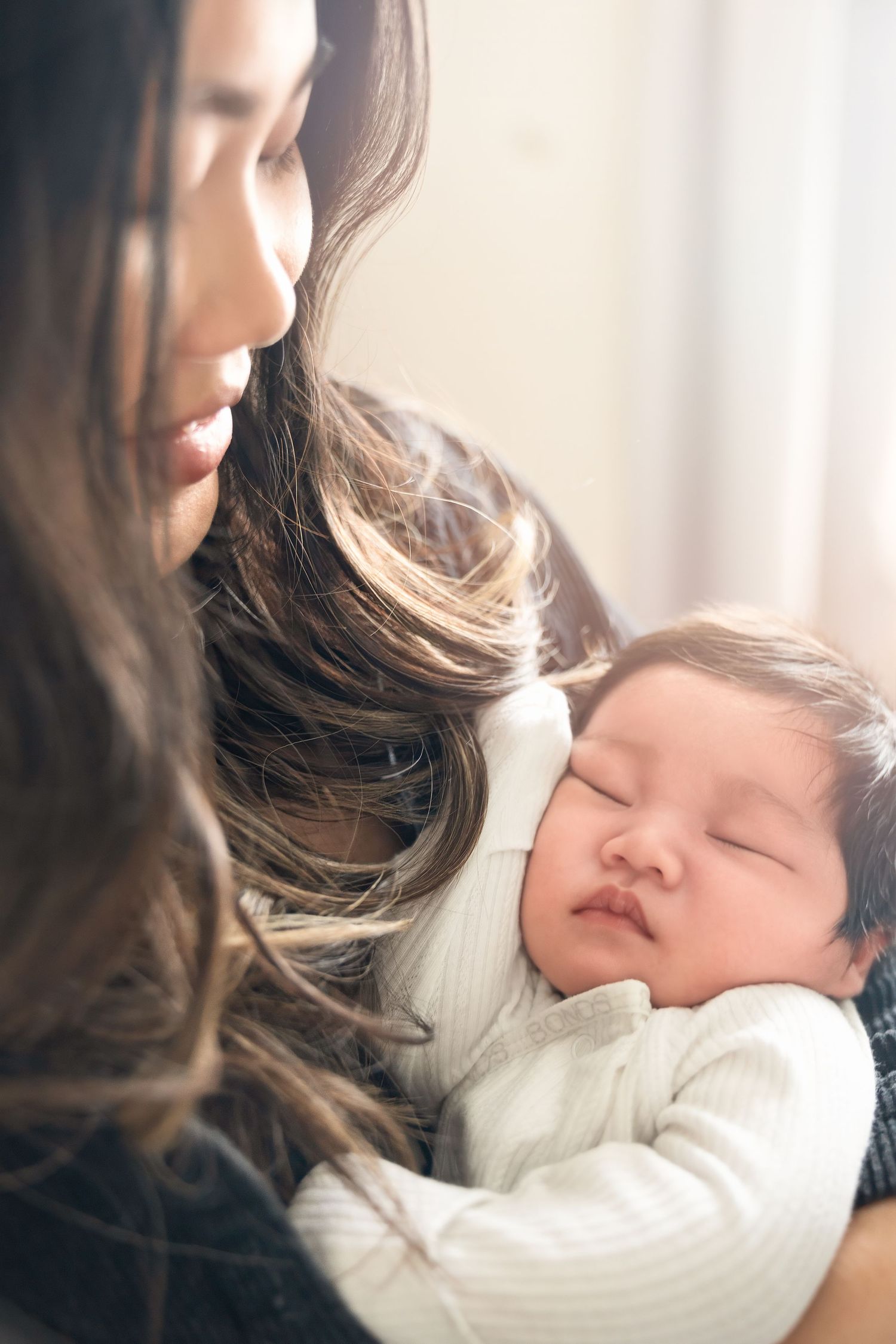 Sleeping newborn in white outfit cradled by parent in tender moment.