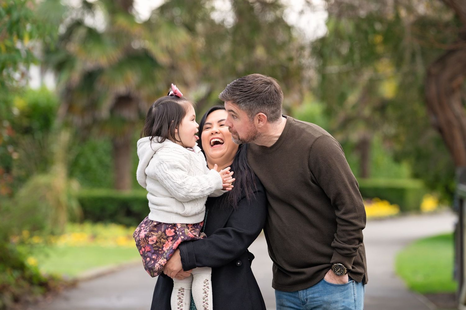 A happy couple laughs and embraces while walking together outdoors on a path surrounded by greenery.