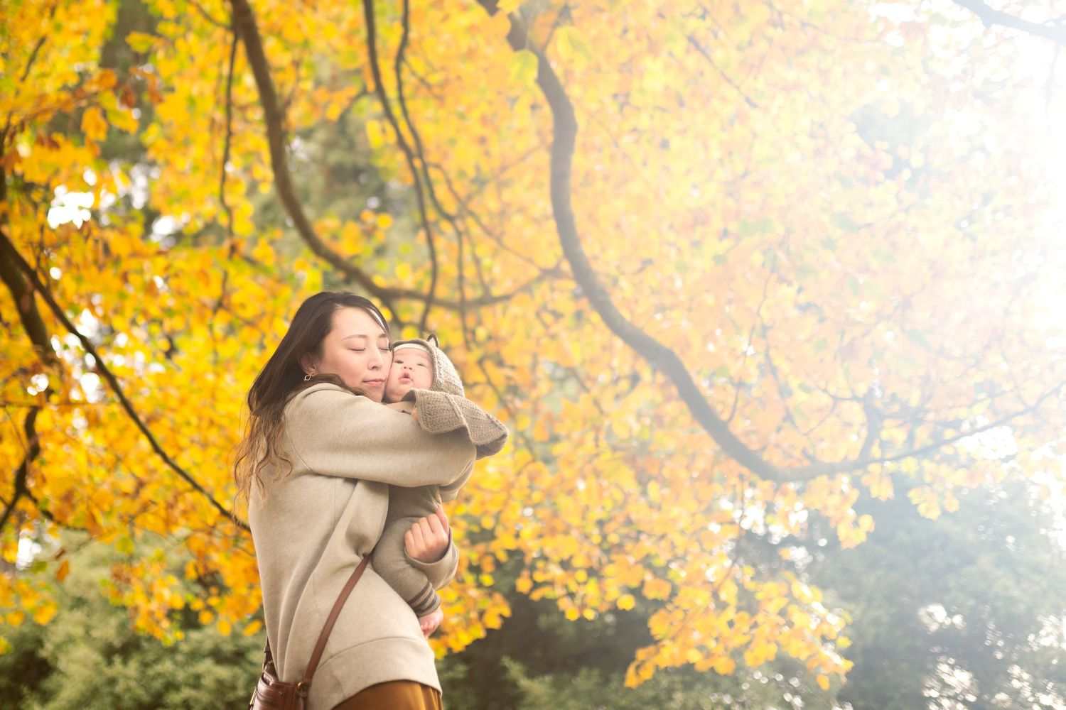 Tender moment shared between parent and child under golden fall leaves in the sunlight.
