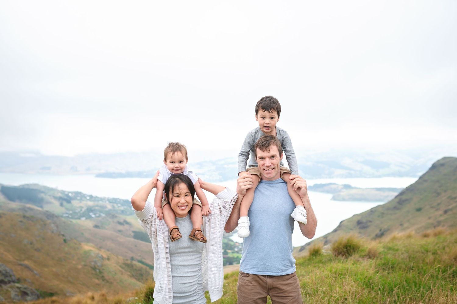 Family giving shoulder rides and playing together on hilltop with scenic mountain views.