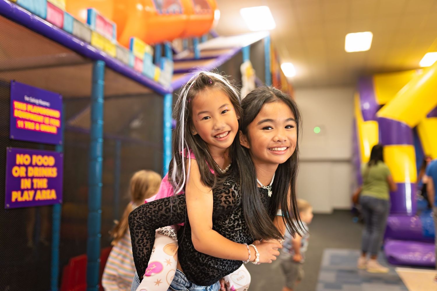 Two young girls smiling and playing in a colorful indoor bounce house play area.