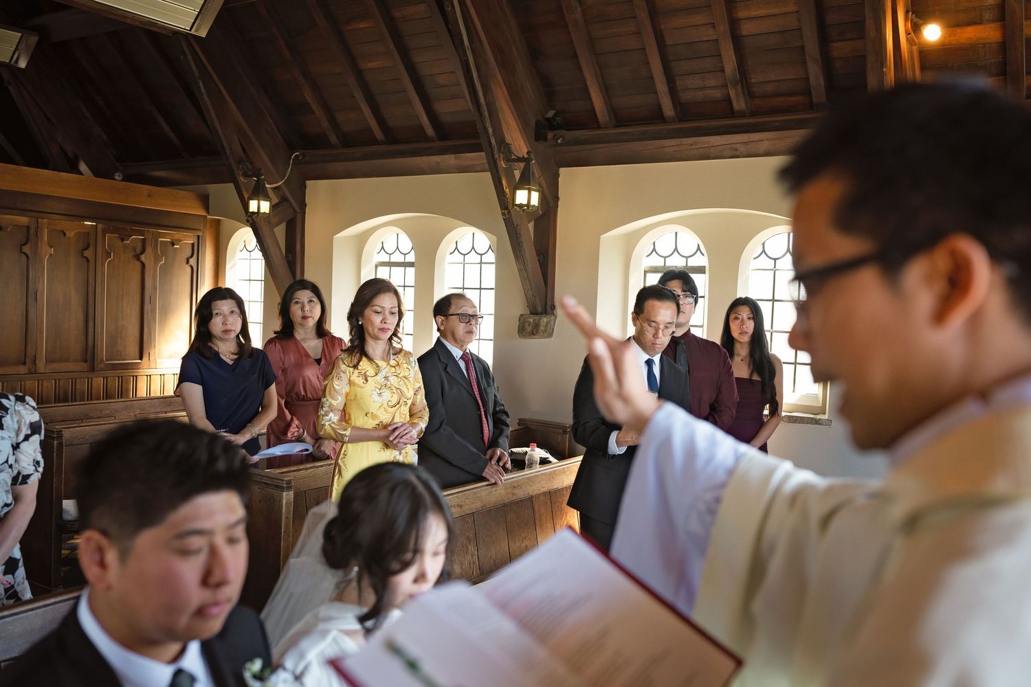 Wedding ceremony inside a charming wooden chapel with guests standing in pews and officiant leading vows.