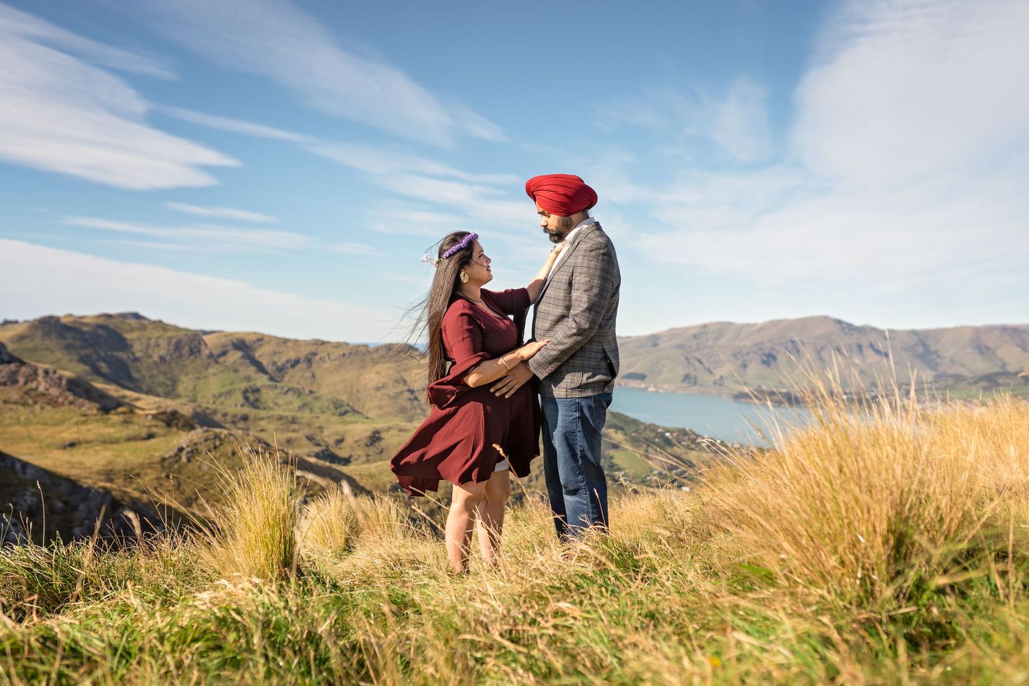 Couple sitting in grassy mountainside overlooking valley during sunny afternoon with blue skies.