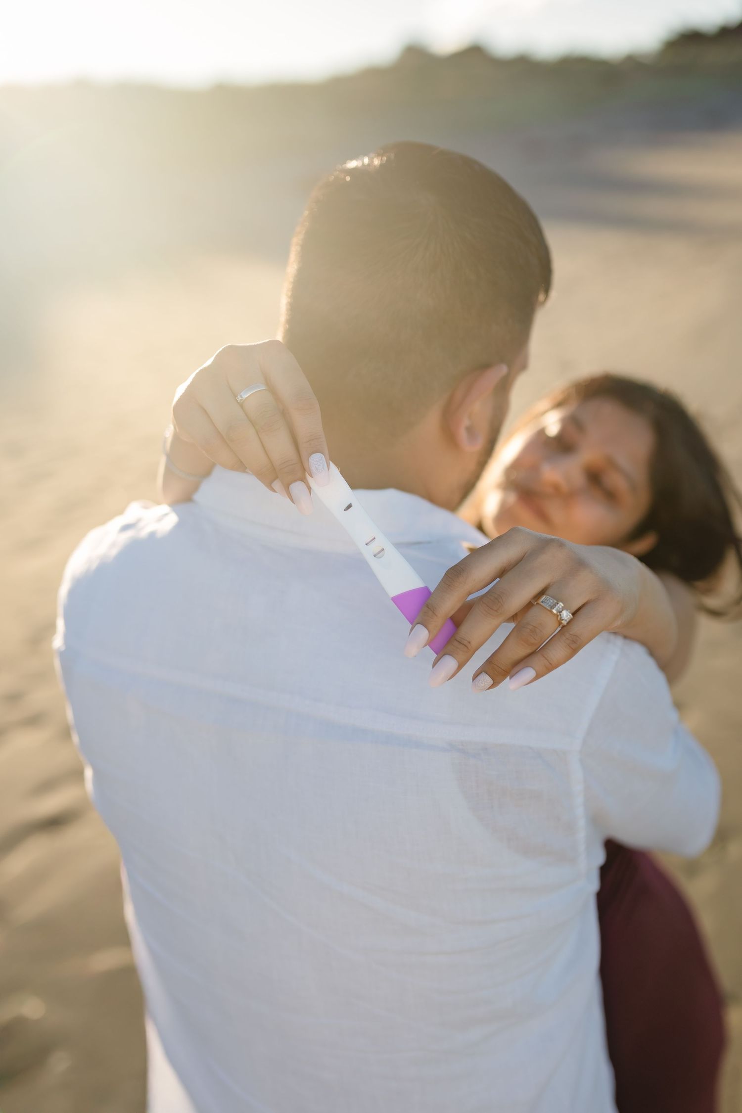 A romantic couple embraces on the beach during golden hour sunlight with glowing backlit atmosphere.