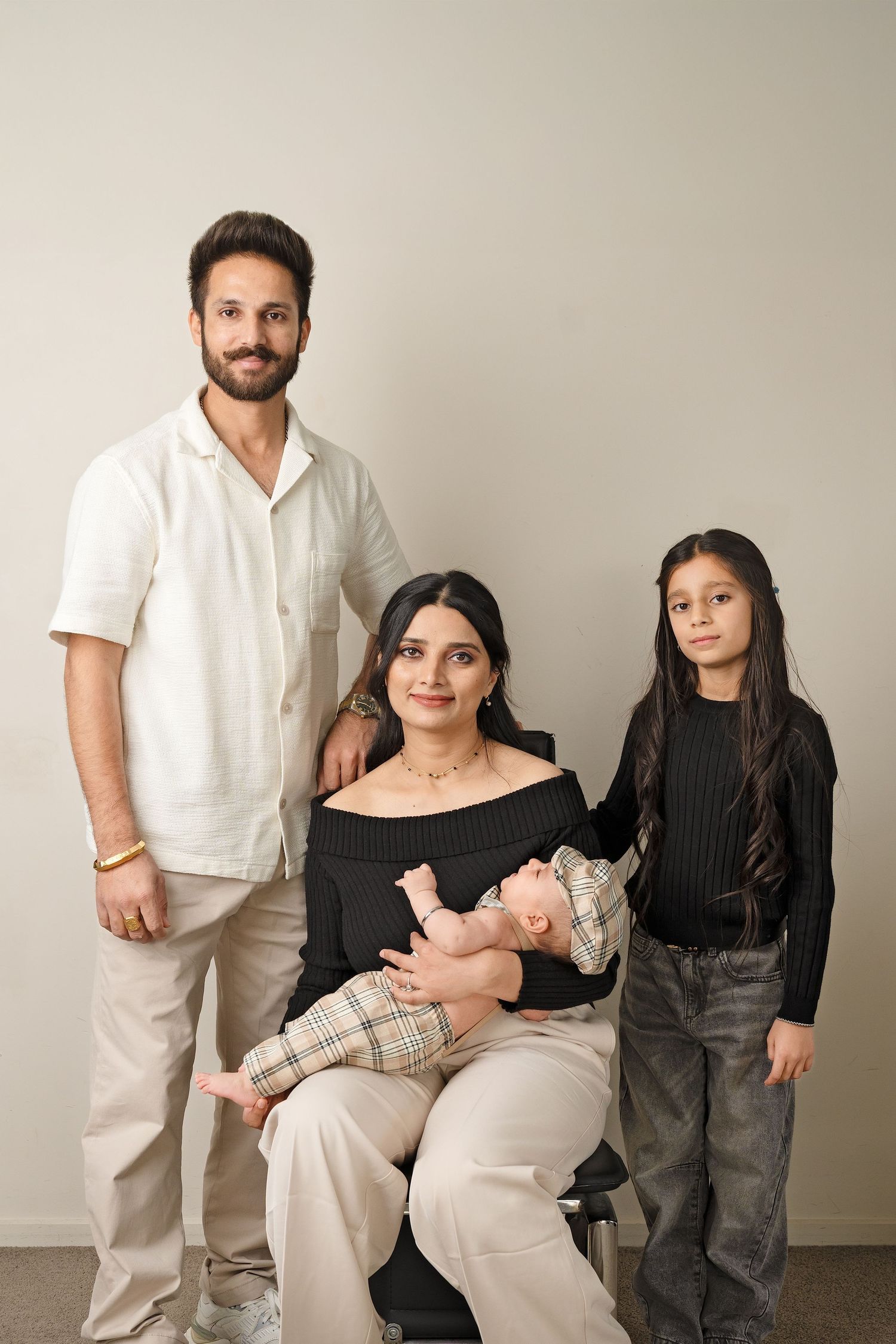 A family group poses in coordinated neutral outfits against a beige background showing progression of staged portraits.