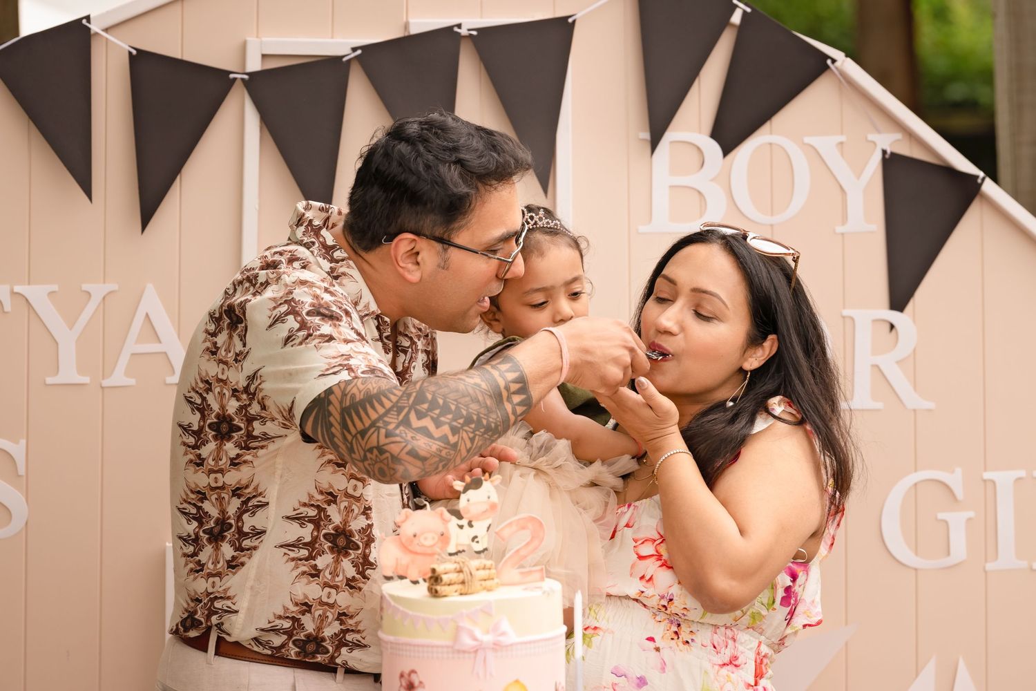 A couple shares a playful moment while feeding each other birthday cake at a party with decorative banners in the background.