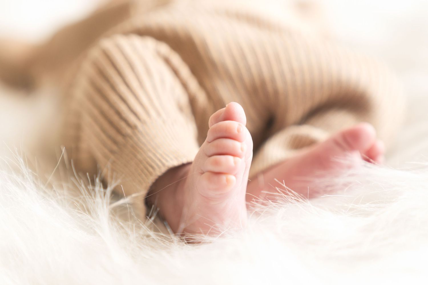 A baby wearing vintage-style glasses and a plaid hat lies on white fabric.
