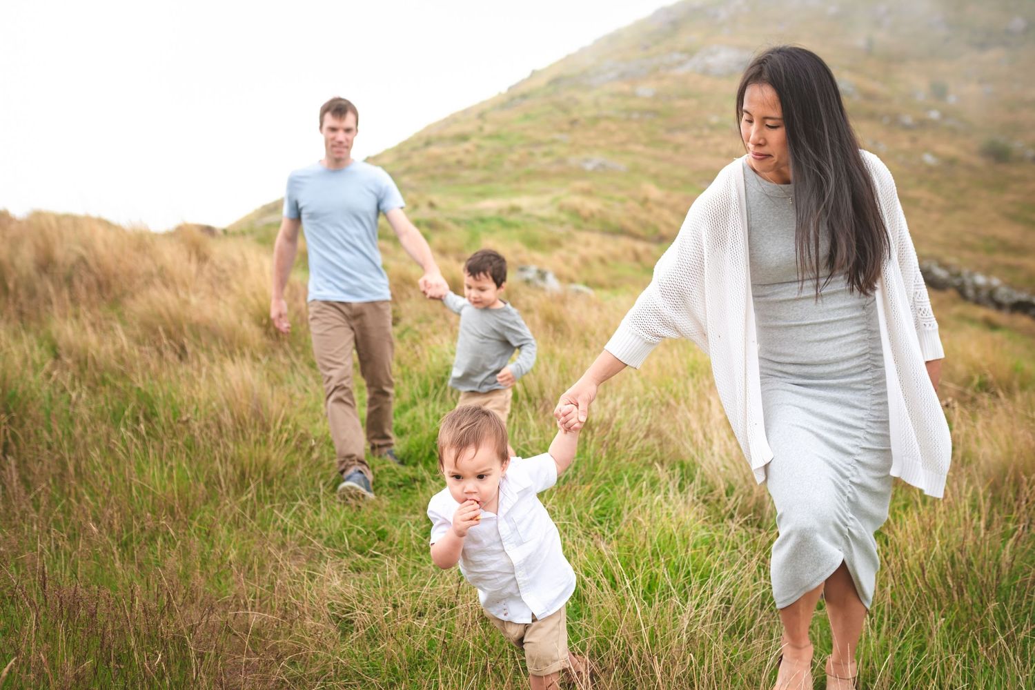 Family walking together through tall grass on scenic mountainside path.