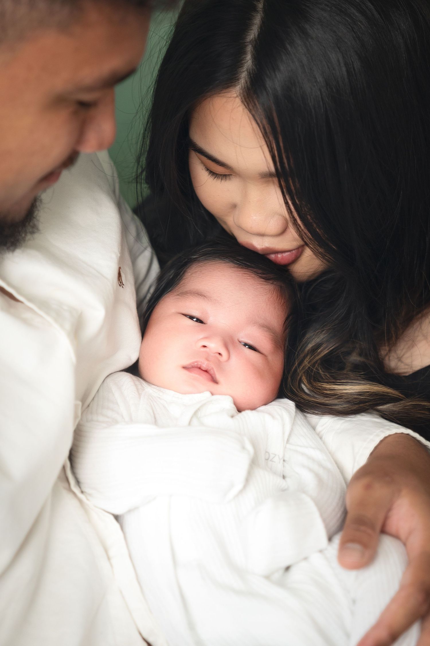 Parents snuggling with their newborn baby in intimate family portrait.