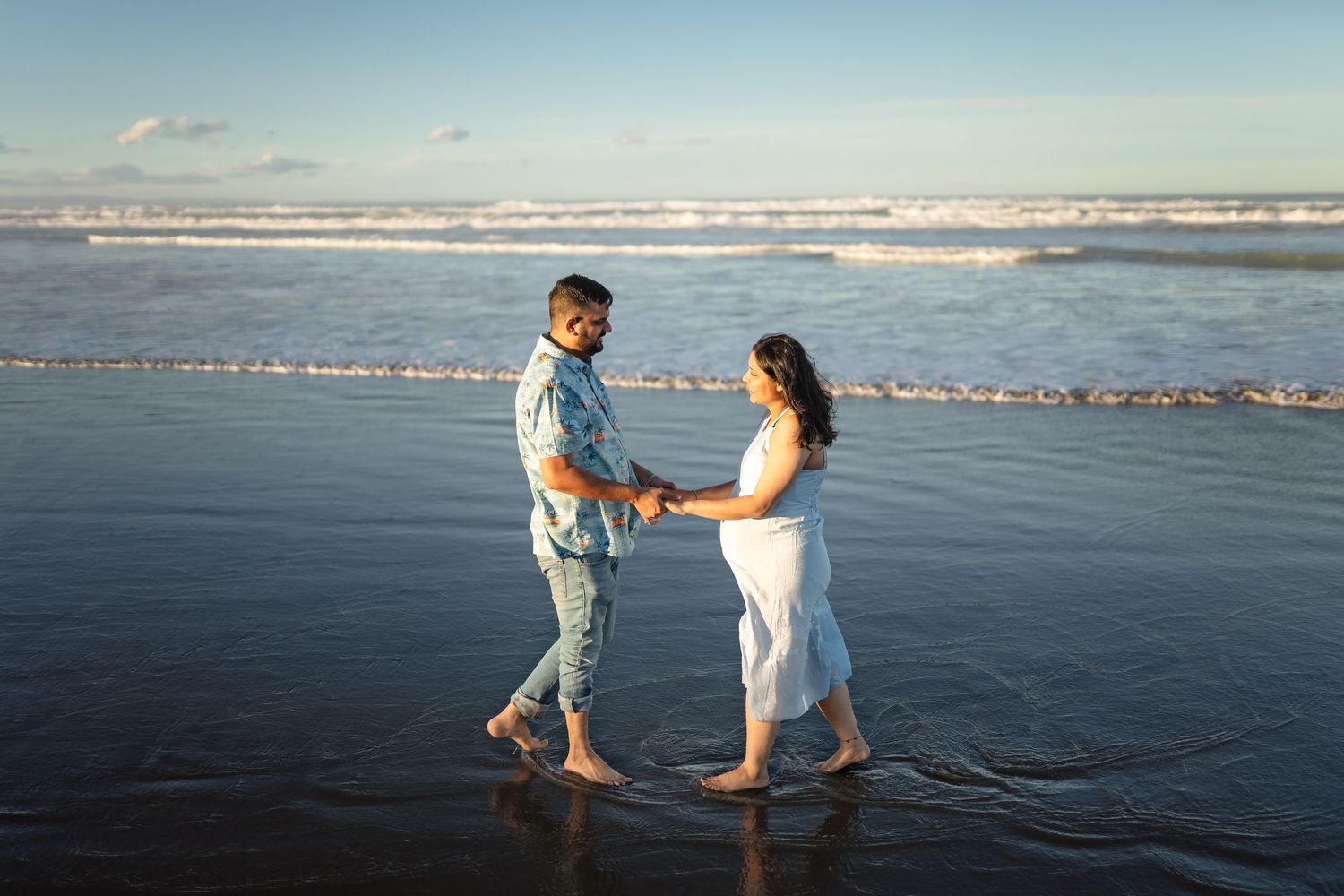 Two people holding hands and dancing together on a dark sandy beach with ocean waves in the background during sunset.
