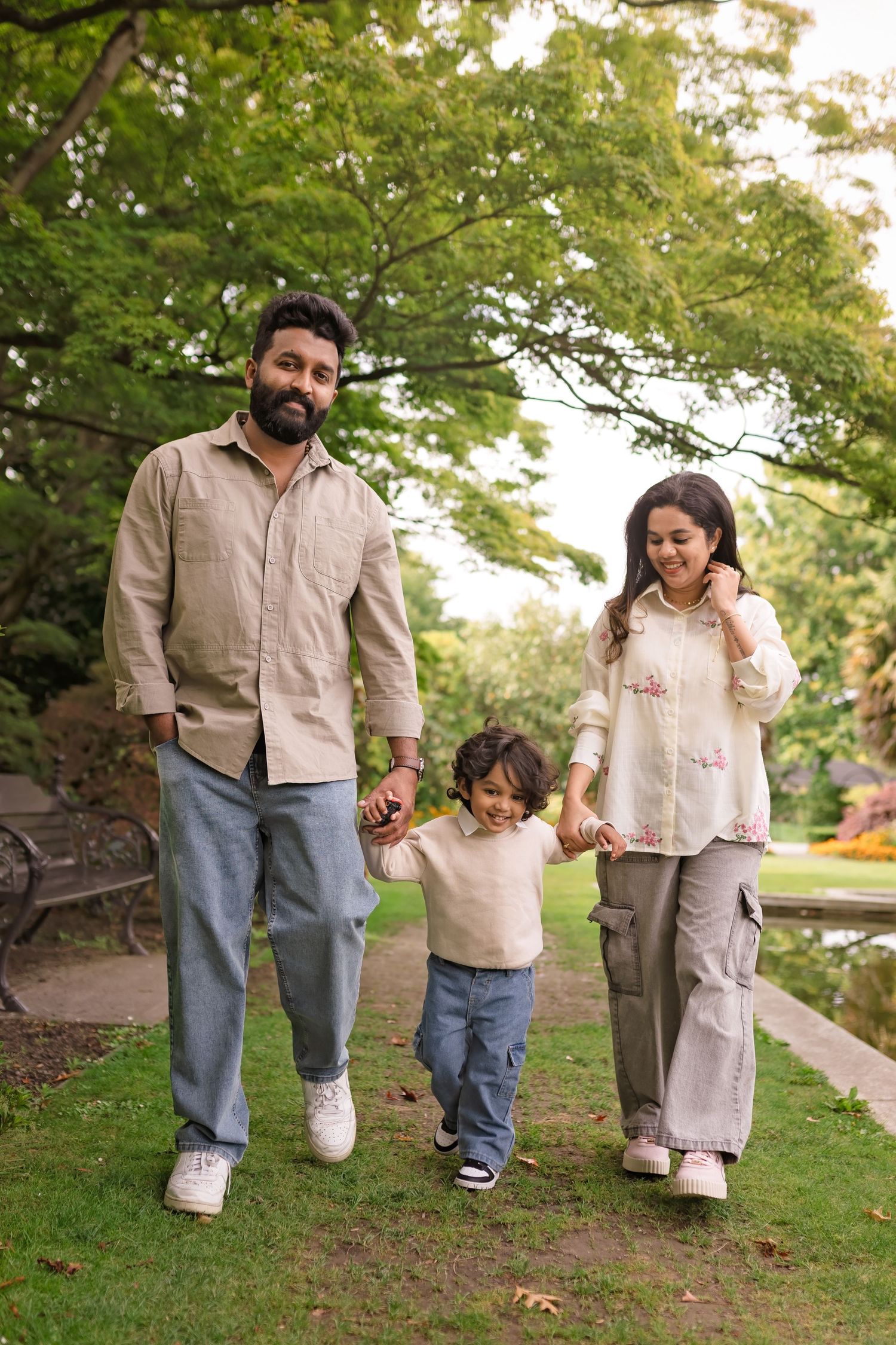 A happy family of three walking hand-in-hand through a lush green park on a sunny day.