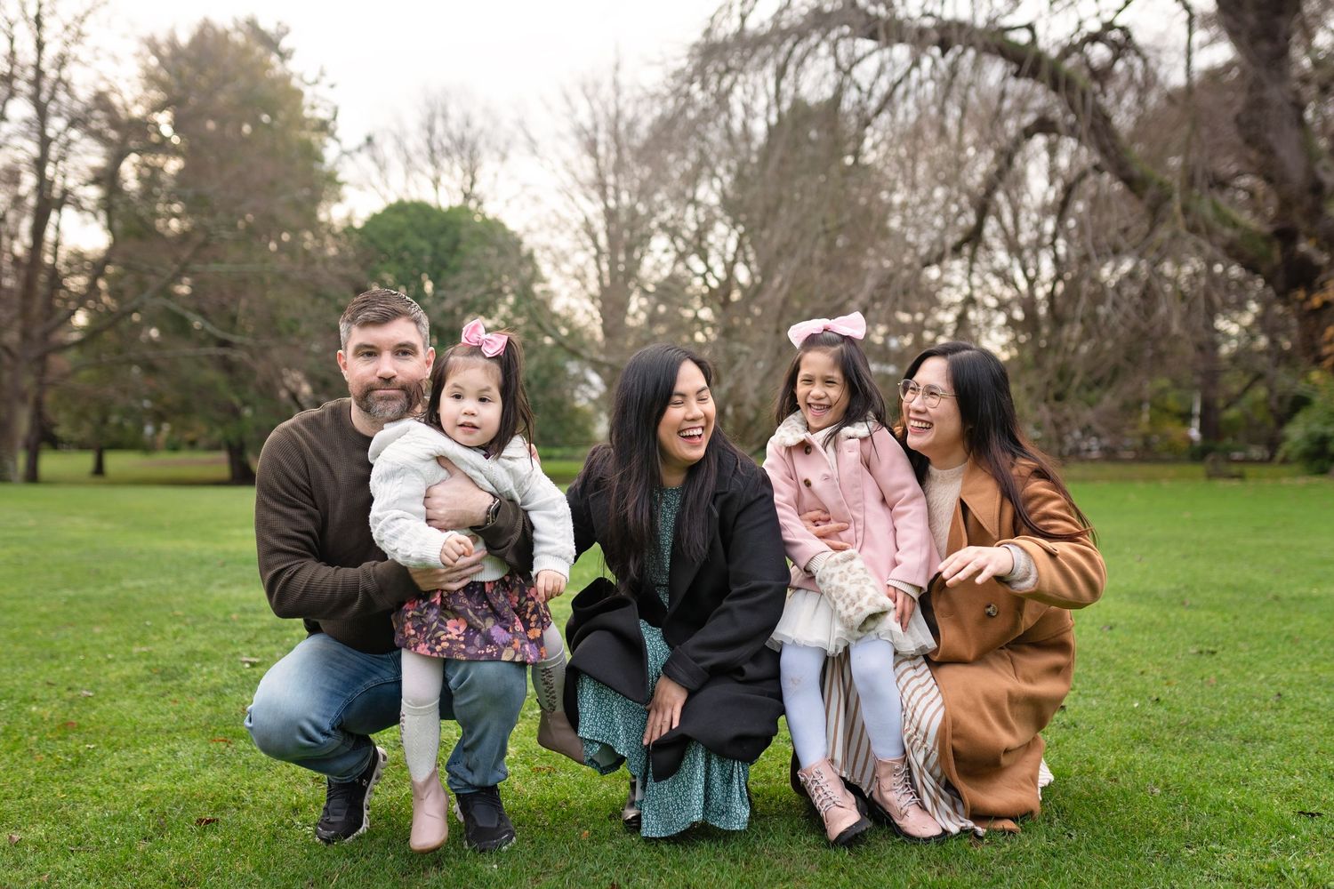 A family plays together on a grassy lawn during a golden autumn afternoon in a park setting.