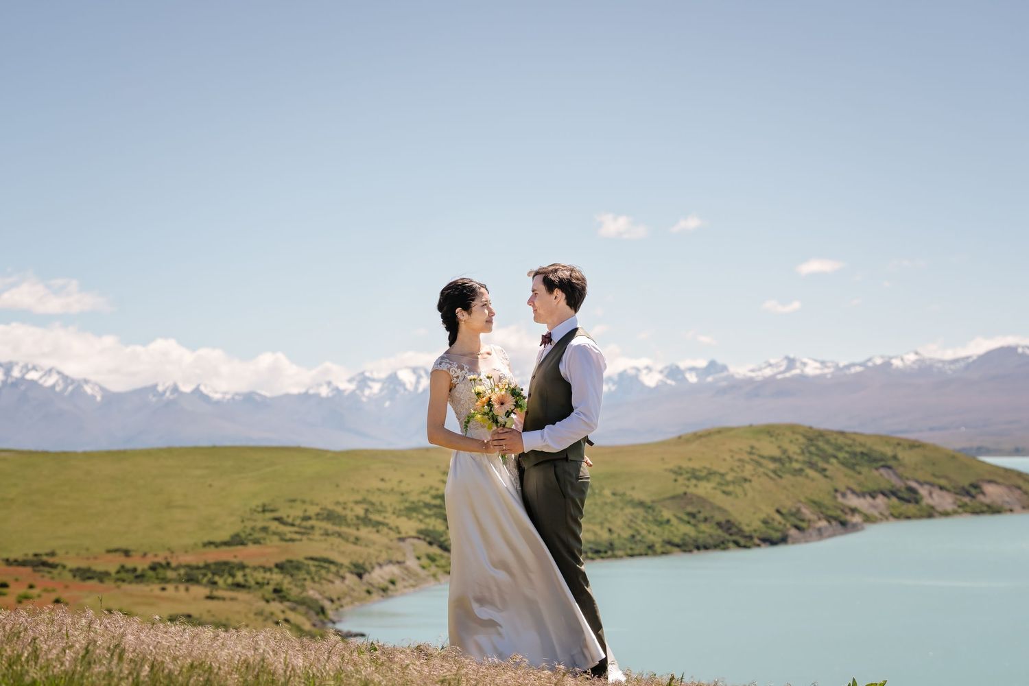 A couple shares a romantic moment at Lake Tekapo in New Zealand with snow-capped mountains in the background.
