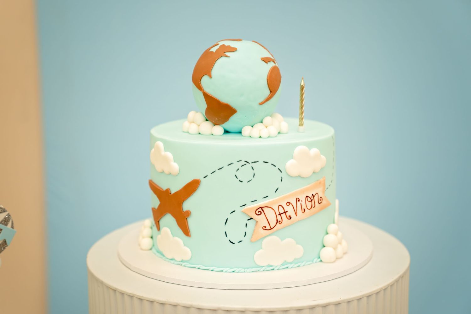 A light blue birthday cake decorated with globe and airplane designs in a travel theme.
