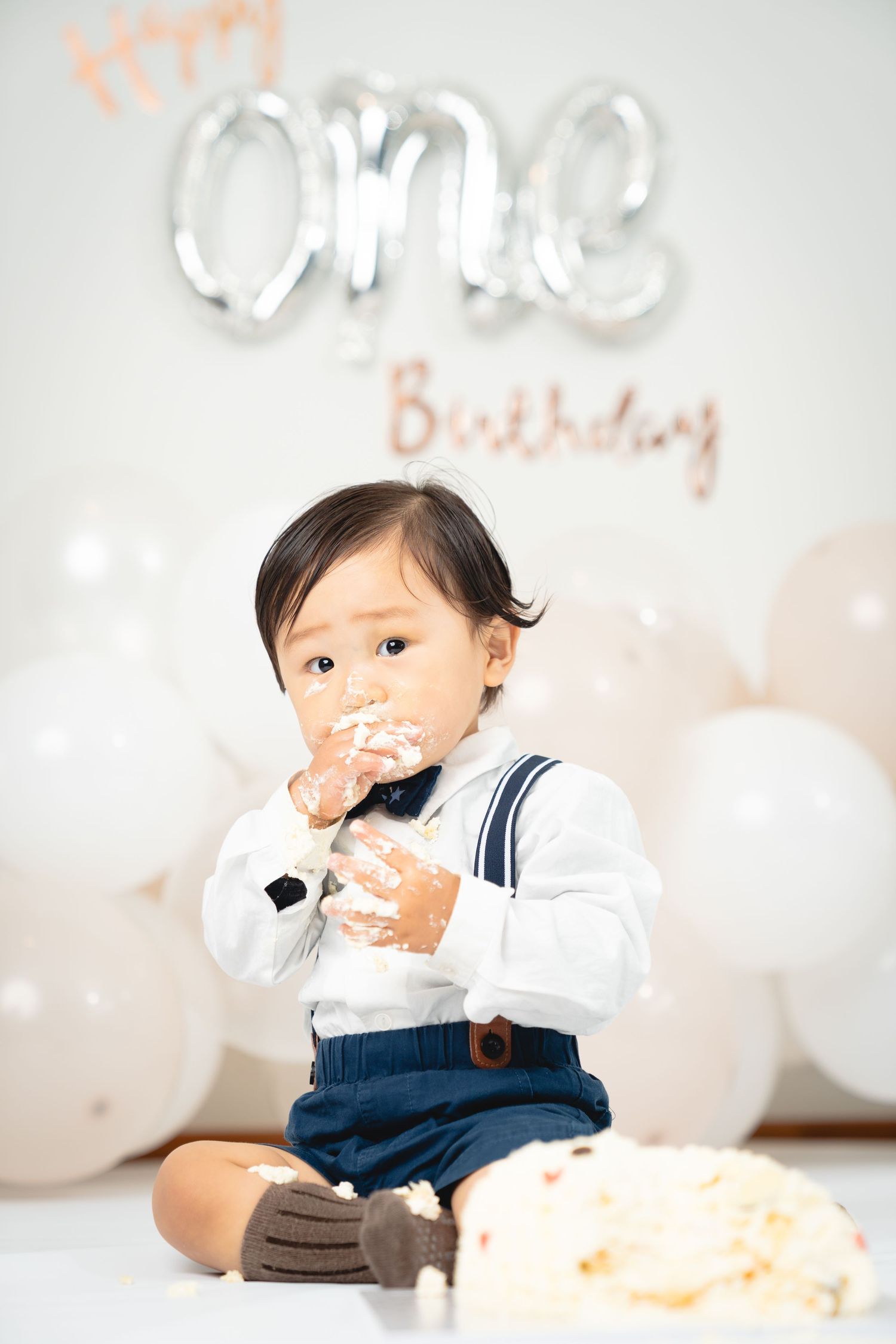 Baby celebrating first birthday with cake smash photo session against balloon backdrop.
