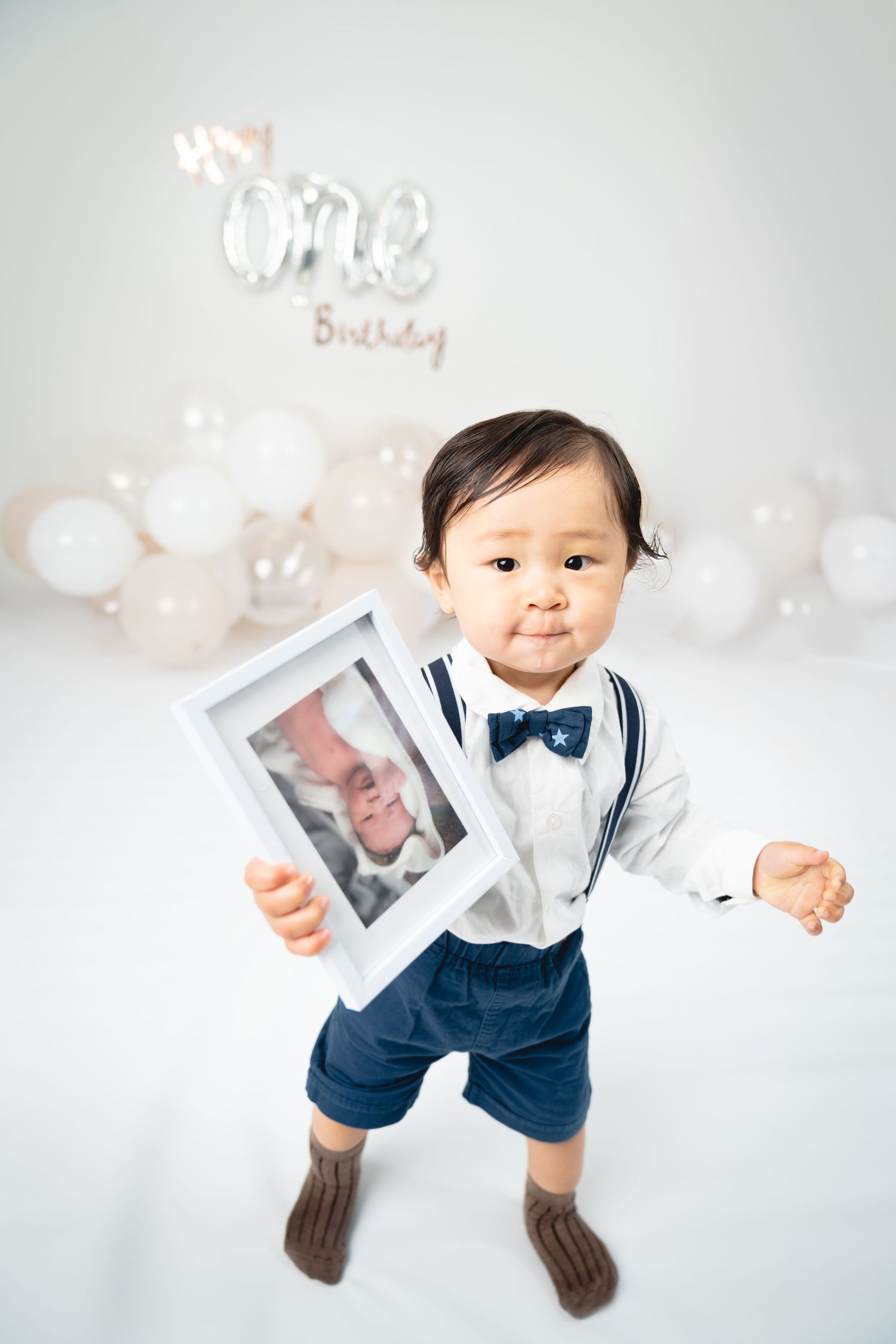 A toddler in formal wear holds up a picture frame during their first birthday celebration.