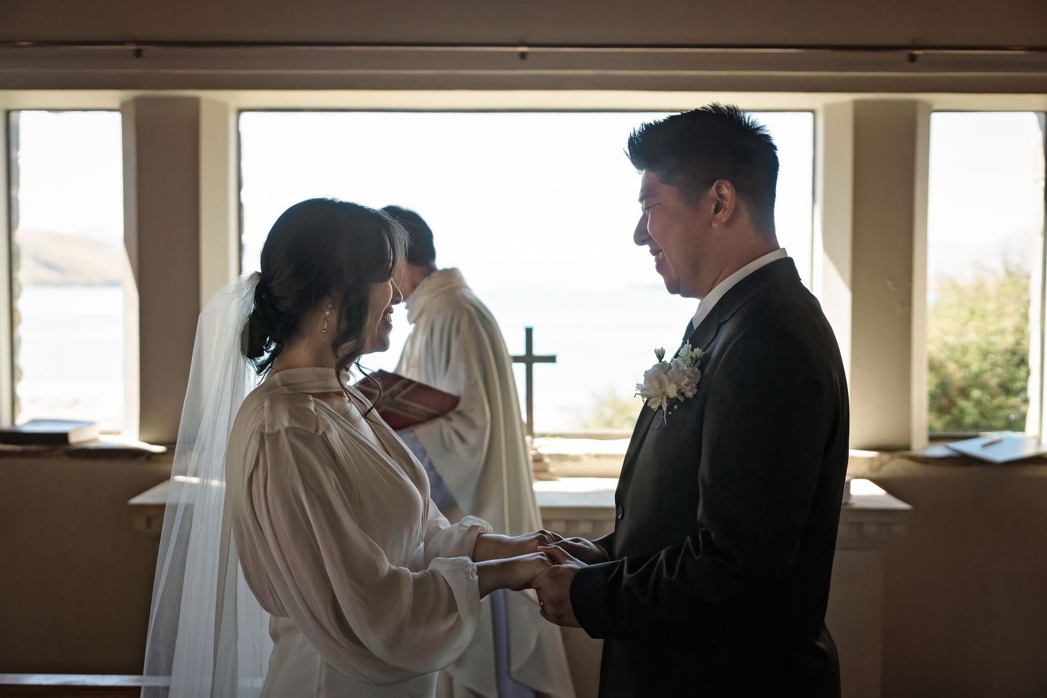Asian bride and groom exchanging vows at chapel window with ocean view.