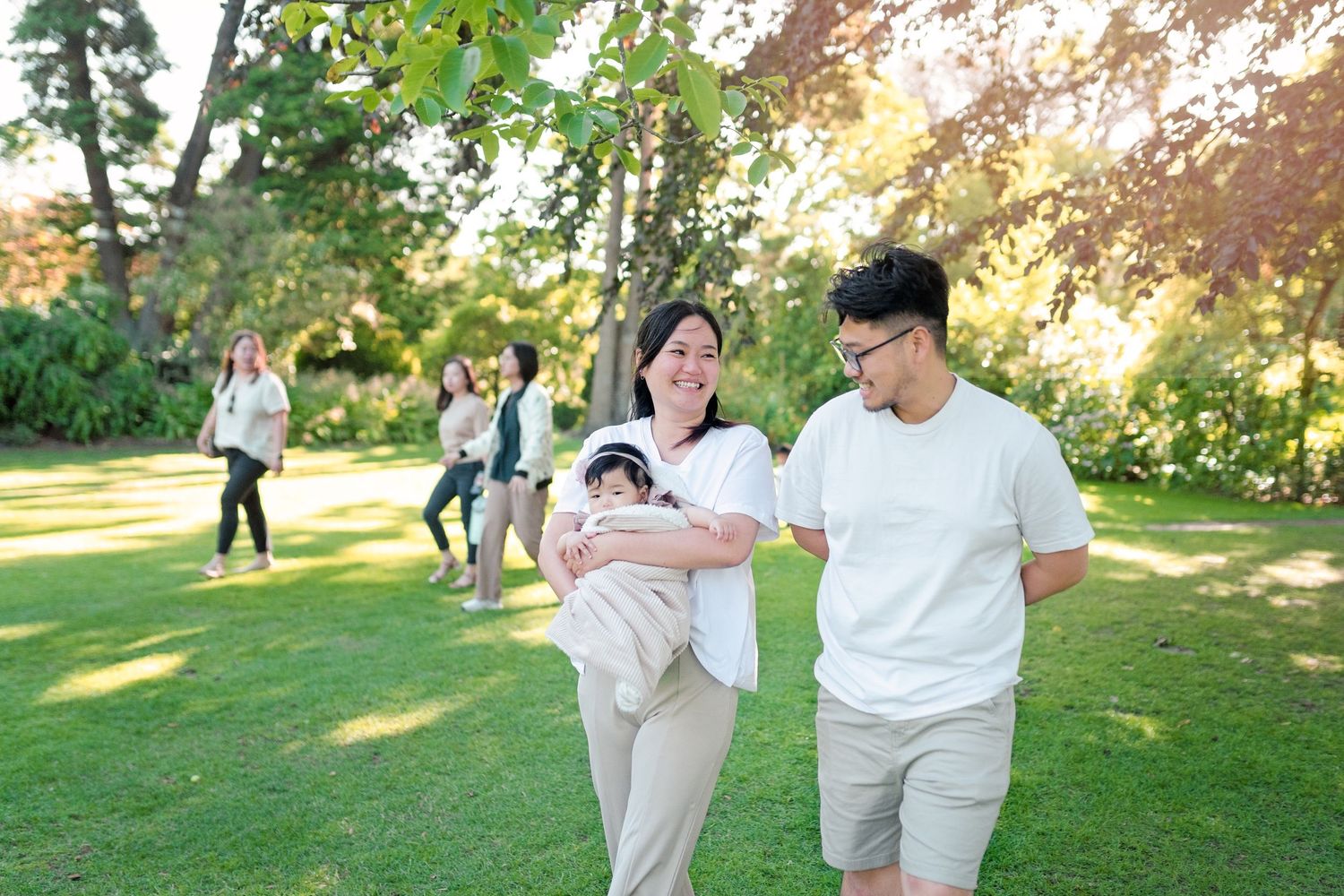 People in light colored clothing walk together in a sunny park setting during an outdoor photo session.