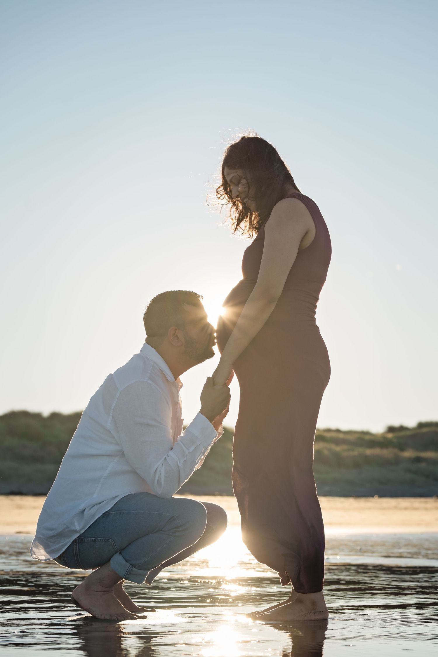 Silhouetted couple shares intimate moment on beach at sunset as sun glows between their figures.