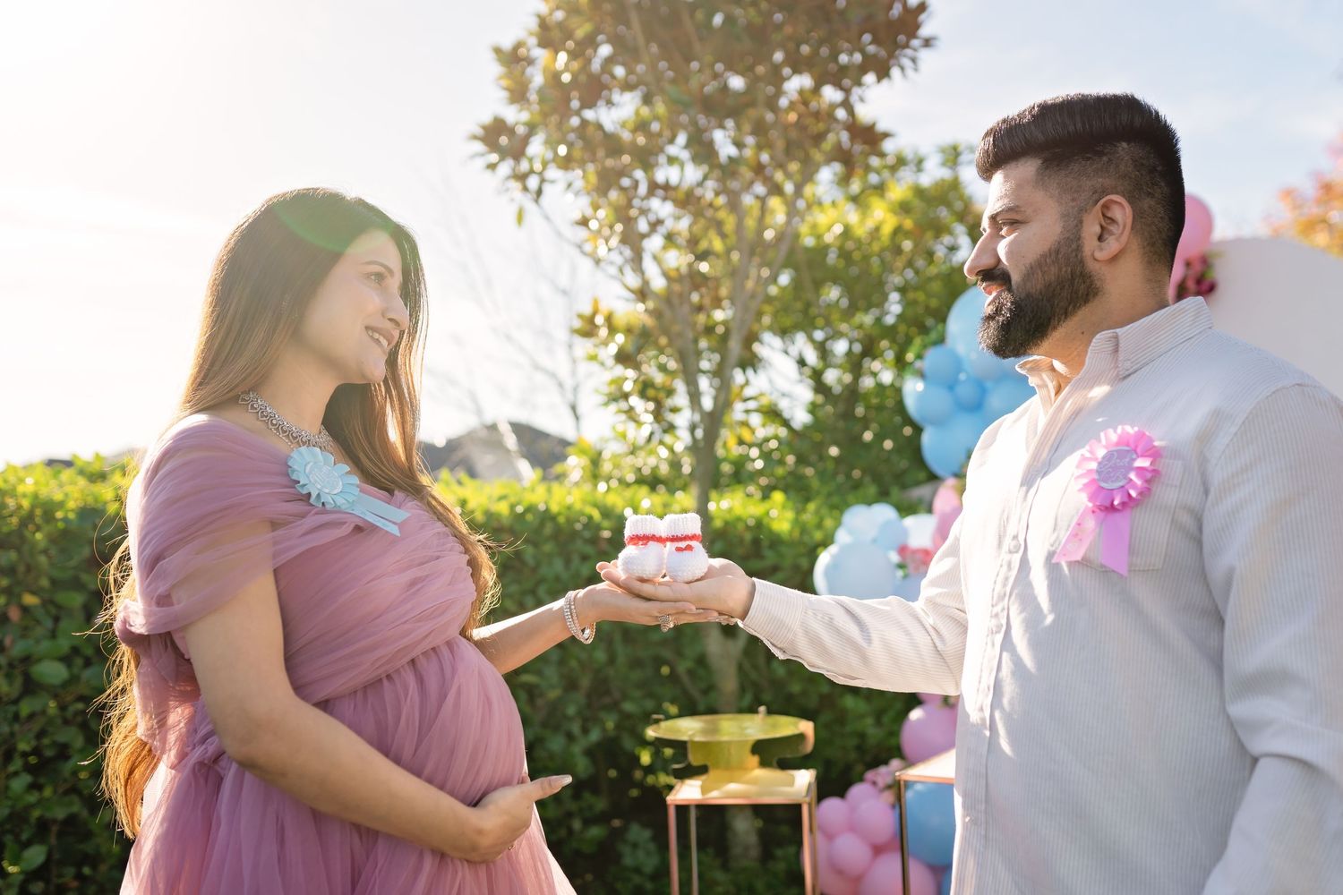 A couple celebrates a gender reveal party outdoors at sunset with pink and blue decorations in a backyard setting.
