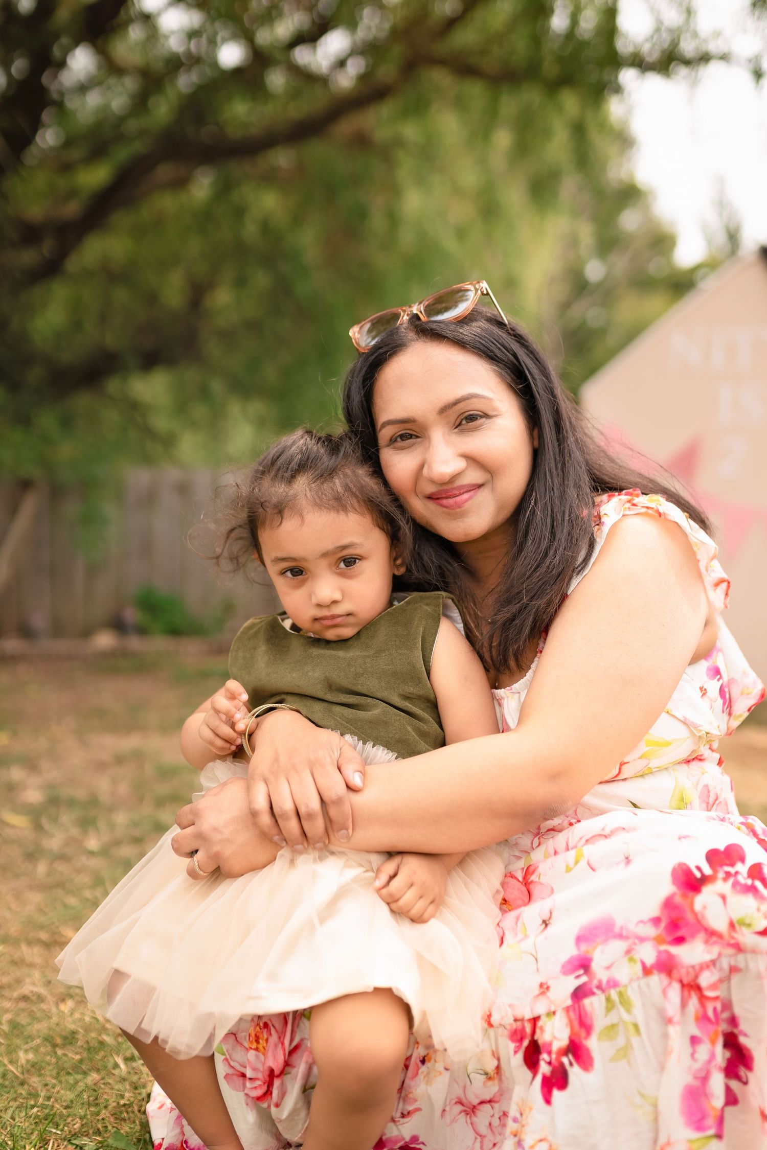 A heartwarming outdoor portrait of a parent and child sitting together on grass in summer attire.