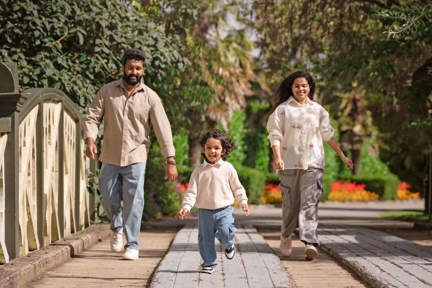 Happy family with young child walking together in a sunny park, holding hands on a brick pathway.