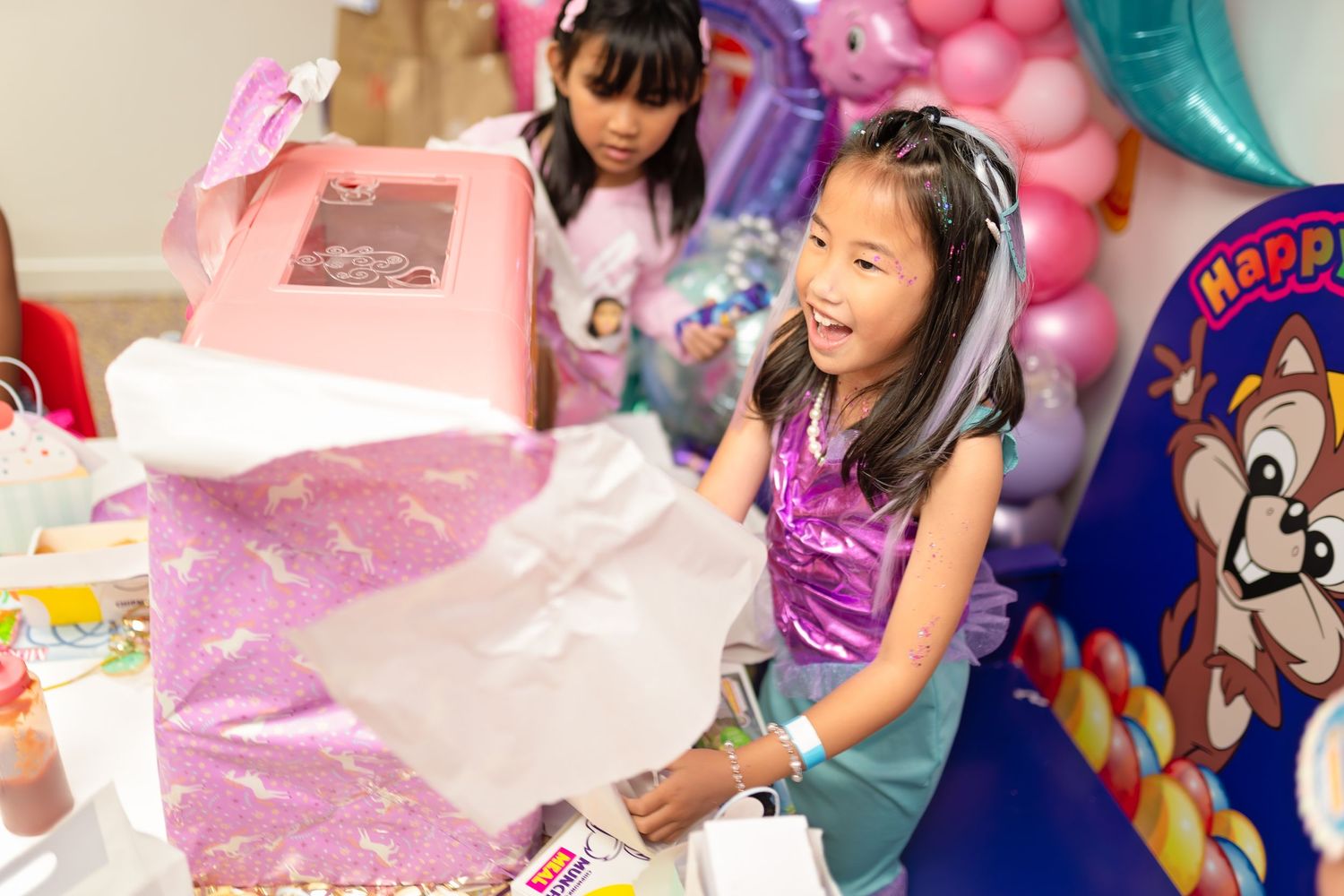 Young girl excitedly unwrapping a pink birthday gift at a colorful Paw Patrol themed birthday party.