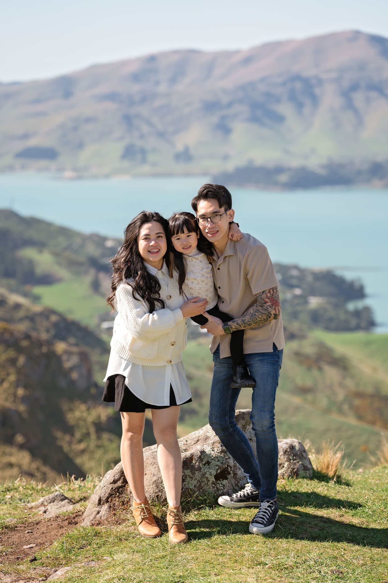 A group stands together on a hilltop overlooking a scenic bay with mountains in the background on a sunny day.